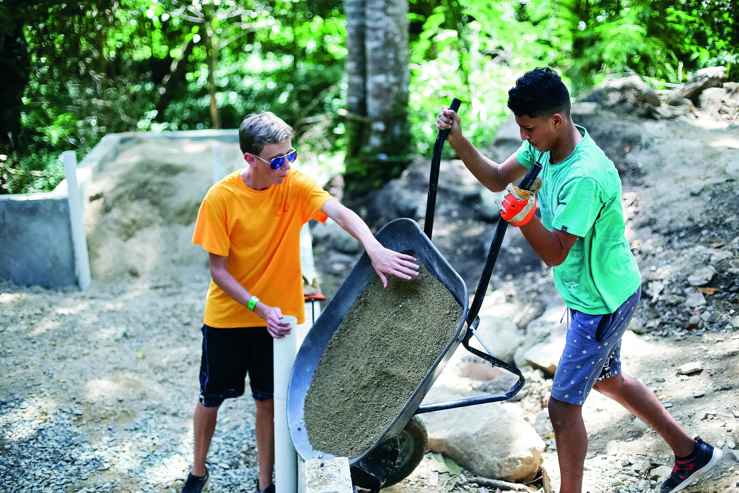 Students push a wheelbarrow of sand at a construction site