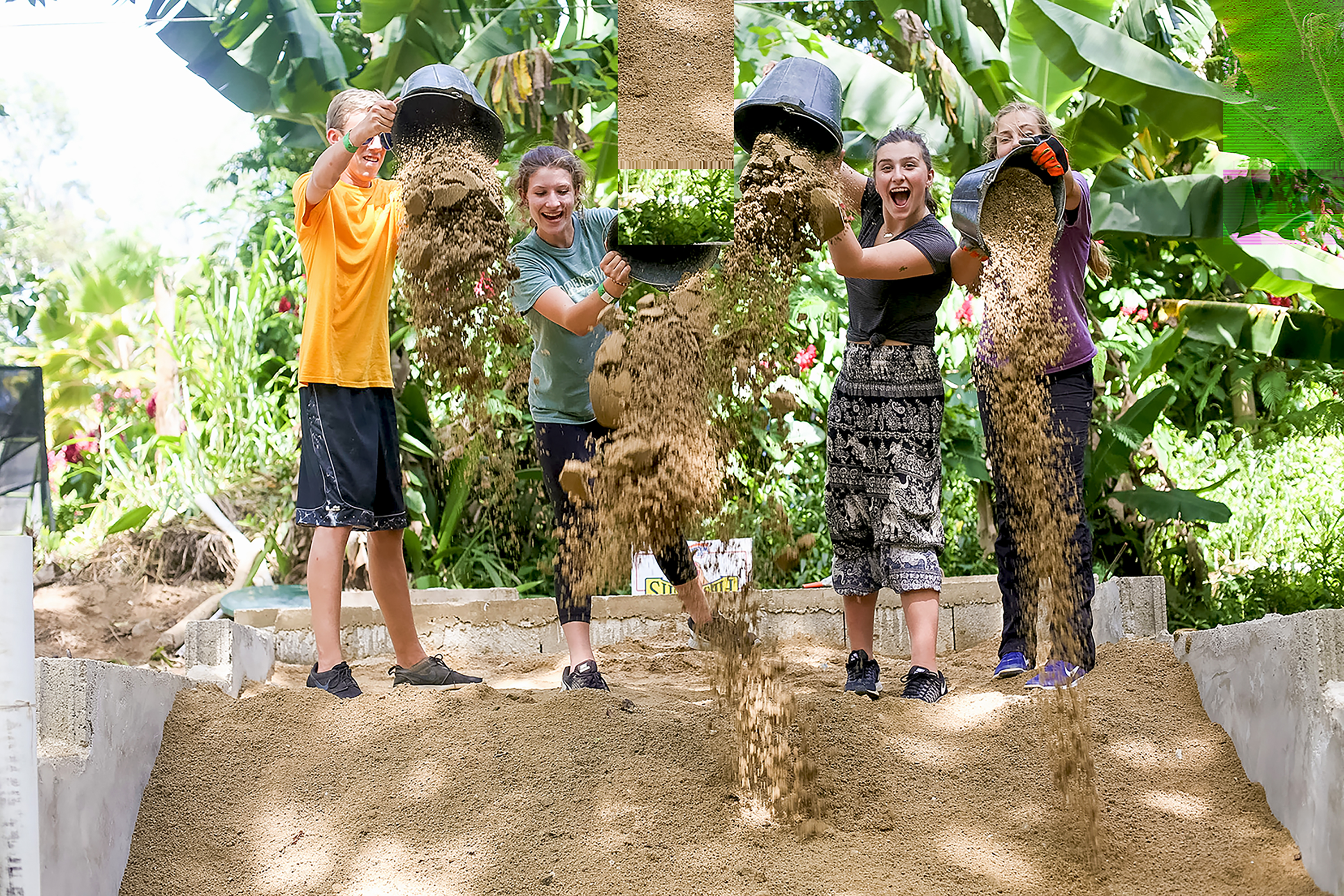 Students dump buckets of dirt down a slope during a service project