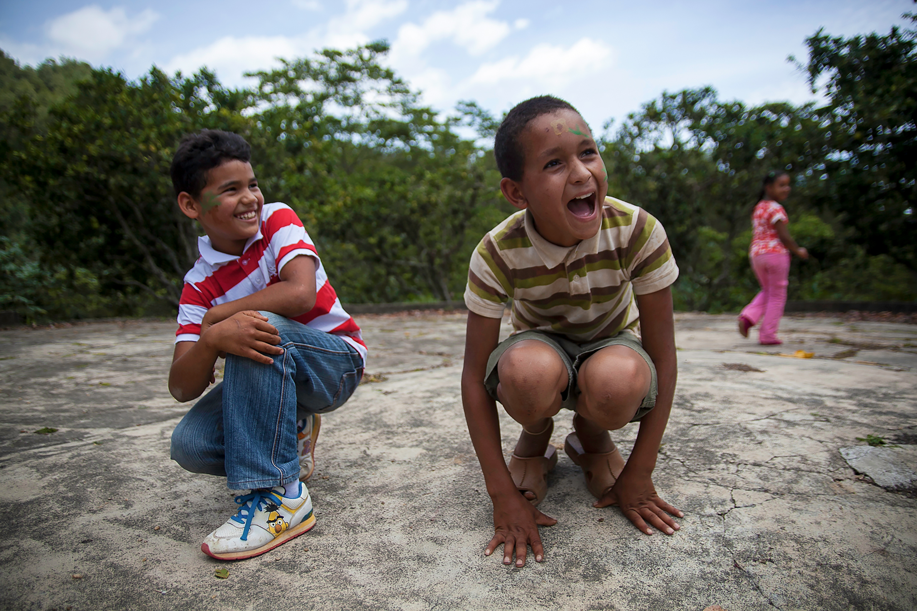 Local children laugh and crouch together on a dirt path in a village