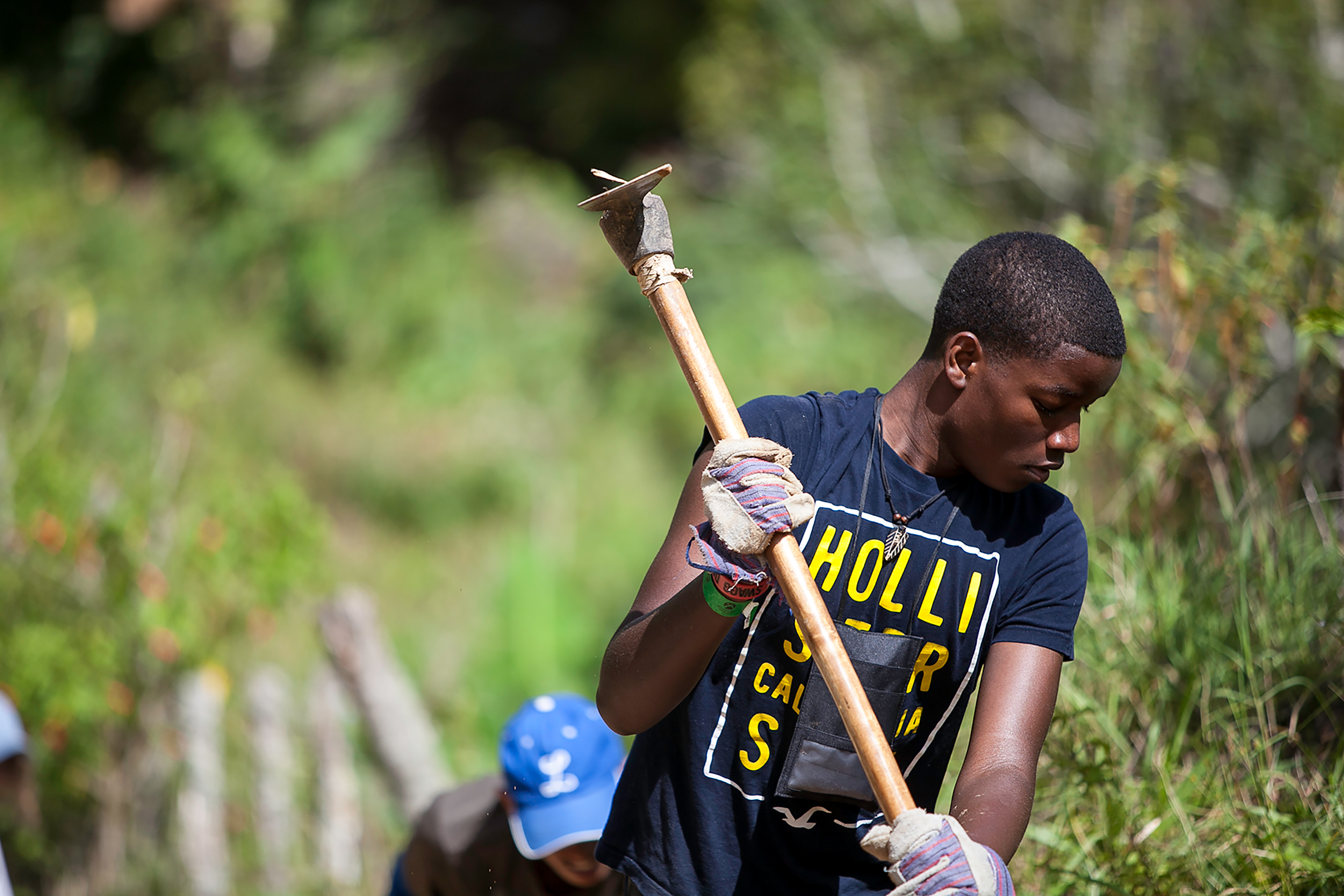 A student wearing work gloves swings a pickaxe during a service project