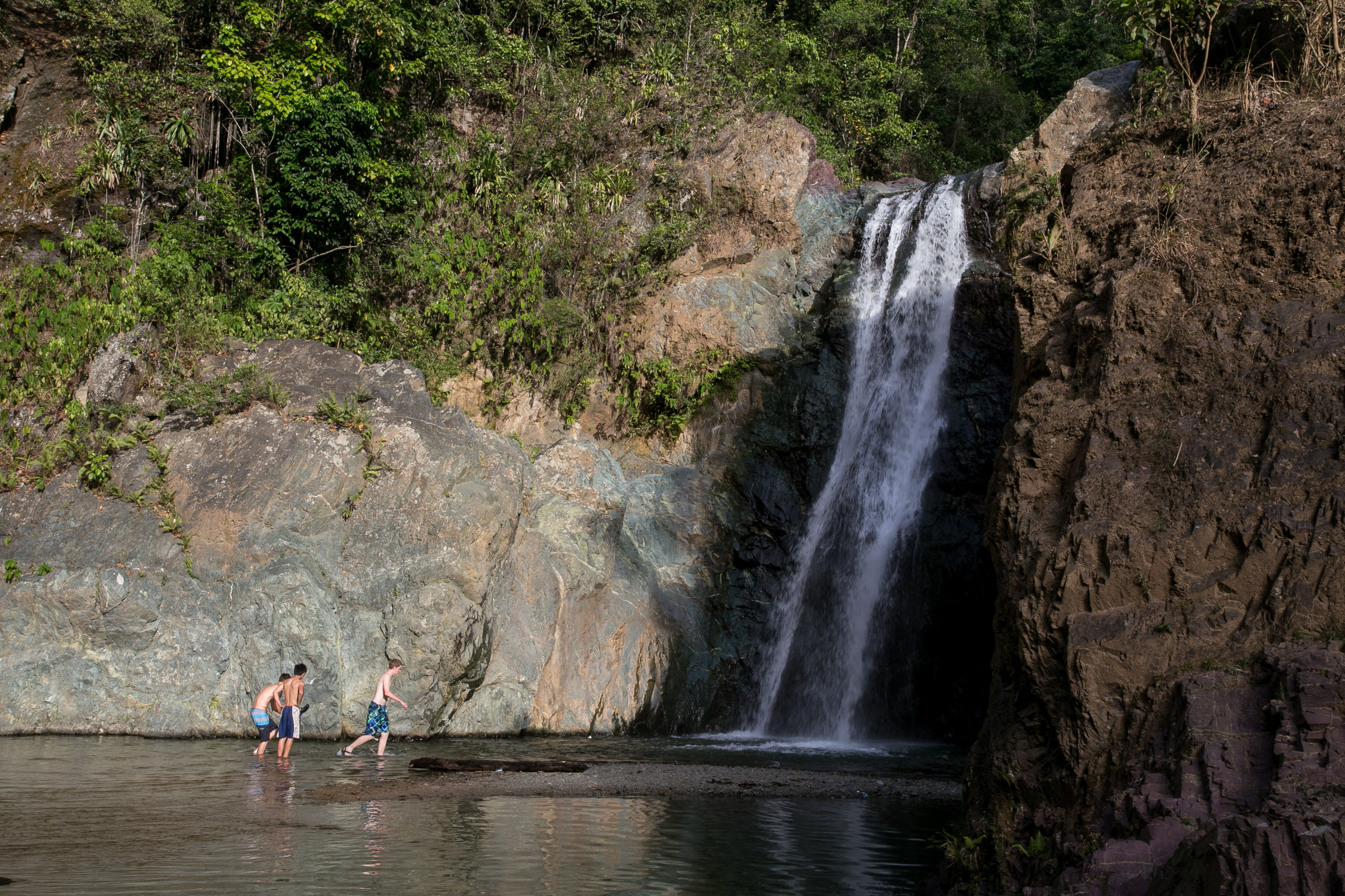 Students wade in a pool at the base of a jungle waterfall
