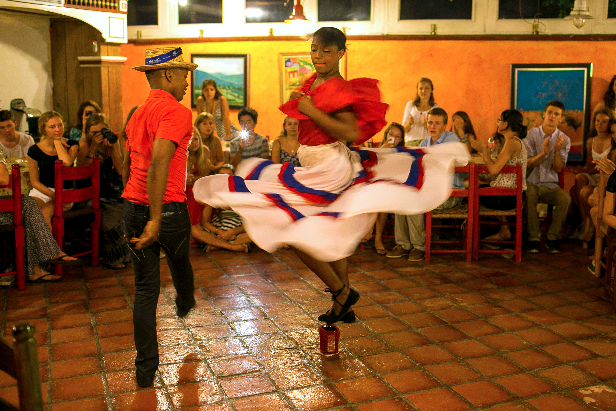 A traditional dancer twirls in a red and white skirted costume as onlookers watch and applaud