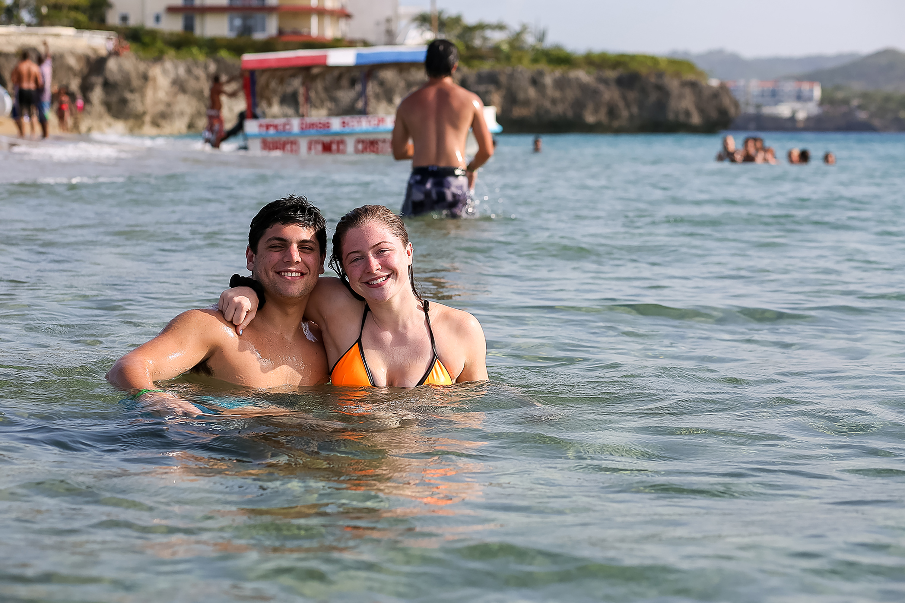 Students wade in calm ocean water near a rocky coastline