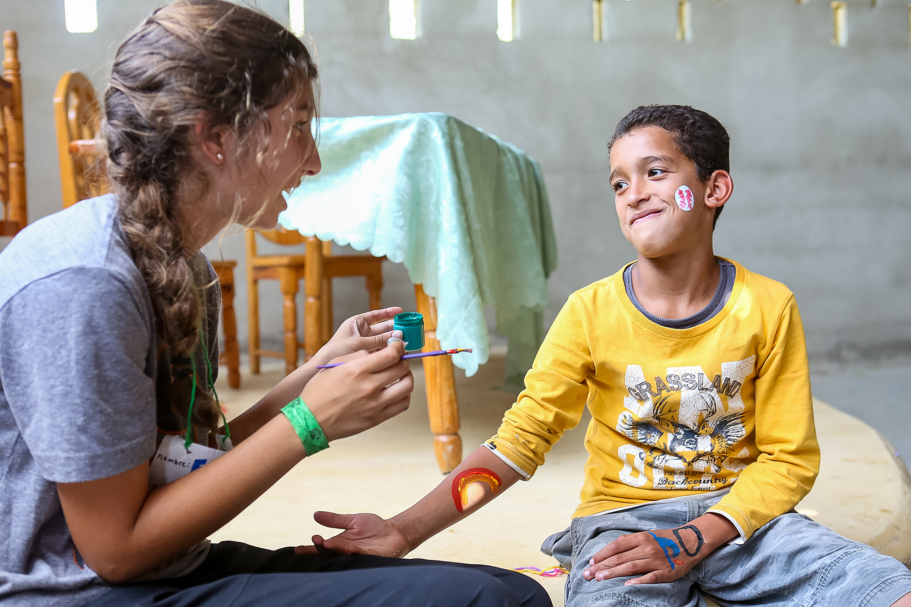 Teens paint a face design on a local child's cheek