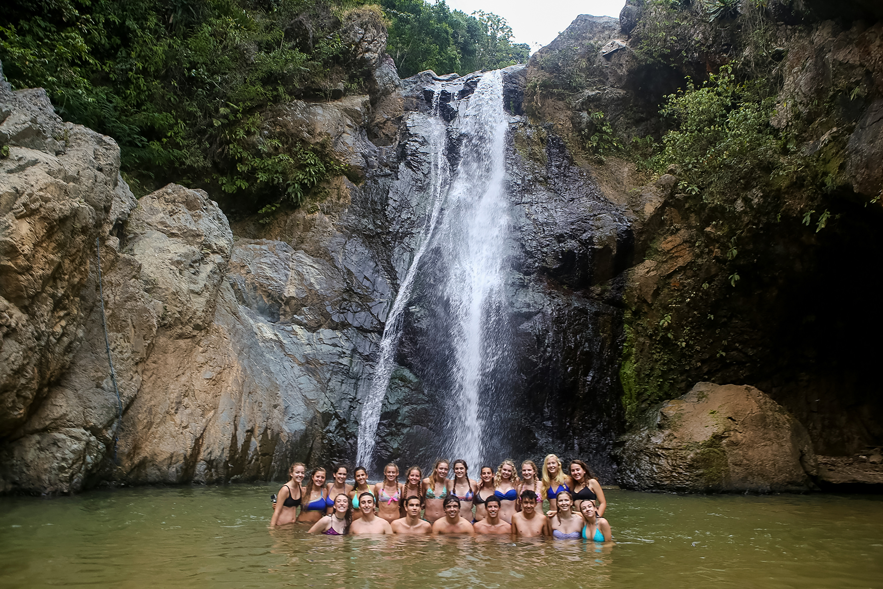 Students wade in a pool at the base of a waterfall