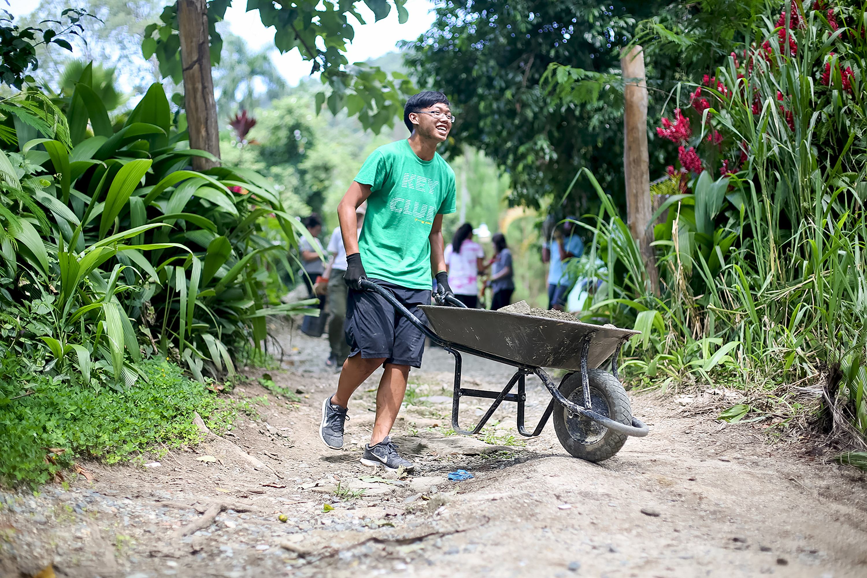 A student pushes a wheelbarrow along a dirt path during a service project in Dominican Republic