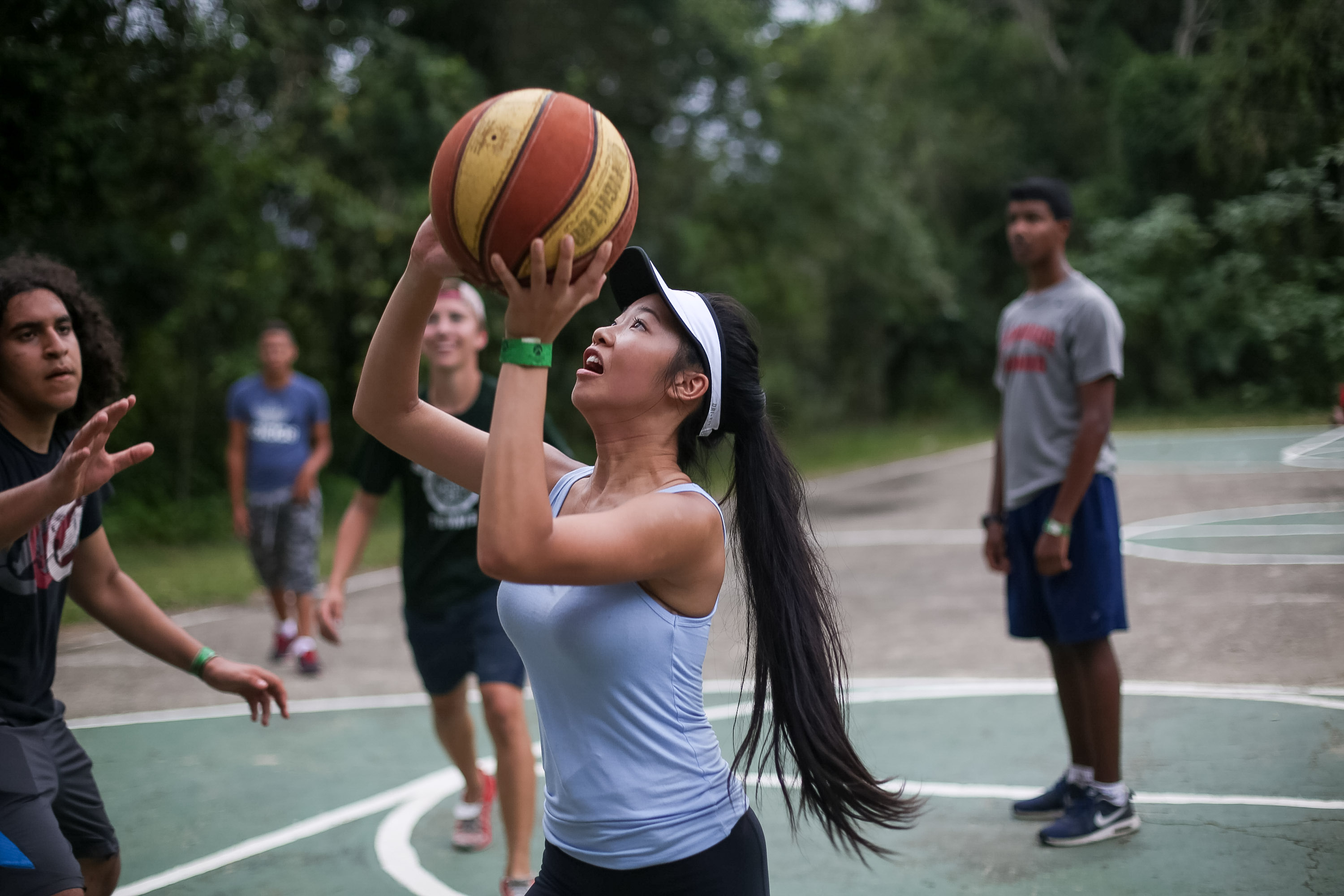 A student shoots a basketball on an outdoor court while others play behind her