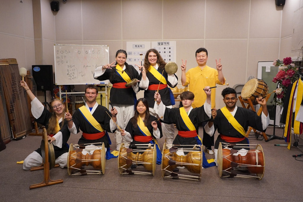 Students wearing traditional Korean clothing try Samulnori, traditional Korean drumming.
