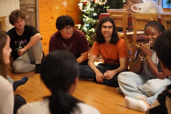 High school students sitting a circle on the floor talking with each other.