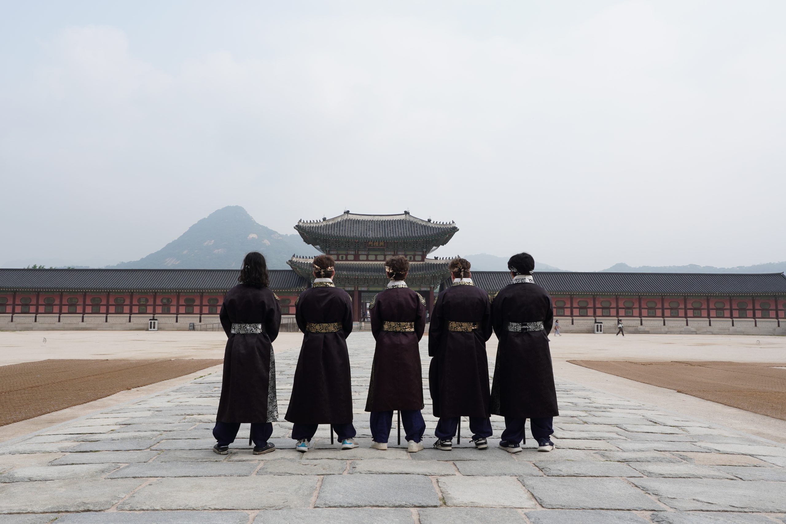 Teens watch as guards in traditional hanbok stand in formation facing Gyeongbokgung Palace