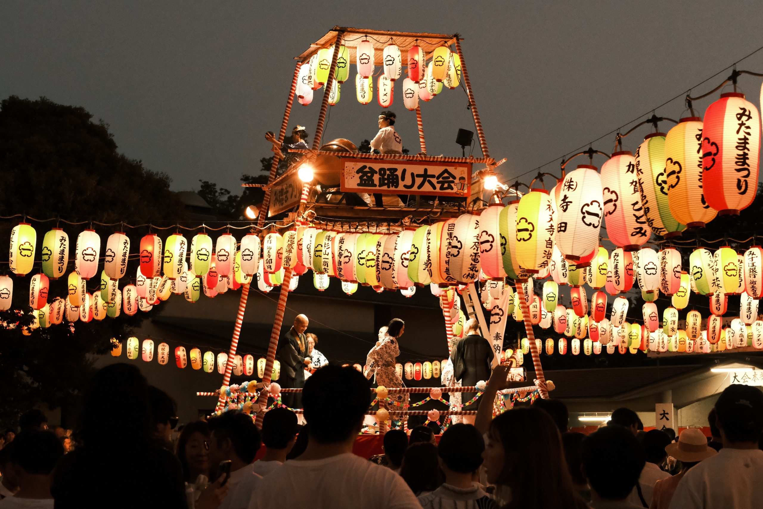 Rows of illuminated paper lanterns hang above a crowd at a nighttime festival in Japan