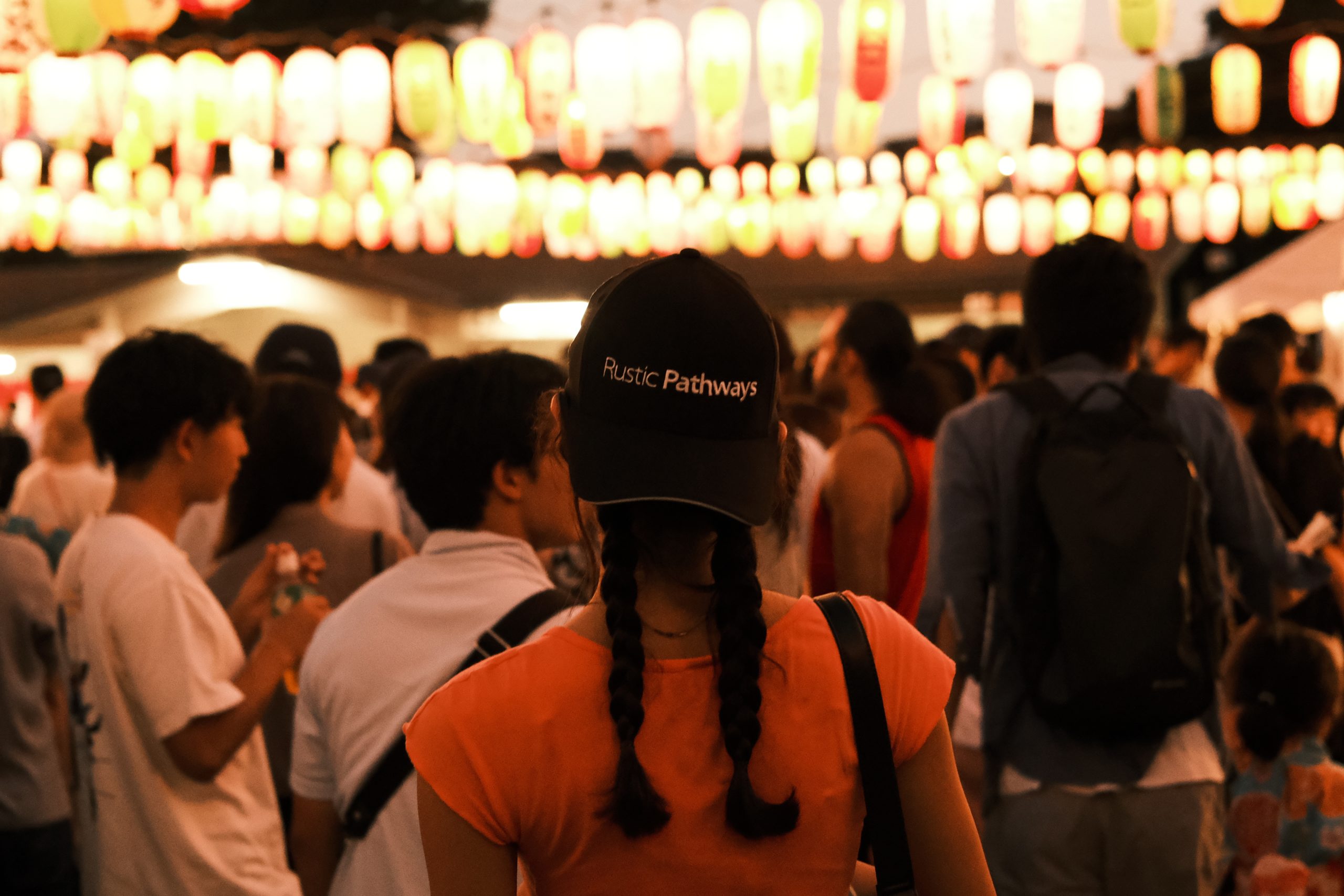 Students wear Rustic Pathways caps under strings of glowing lanterns at a night festival