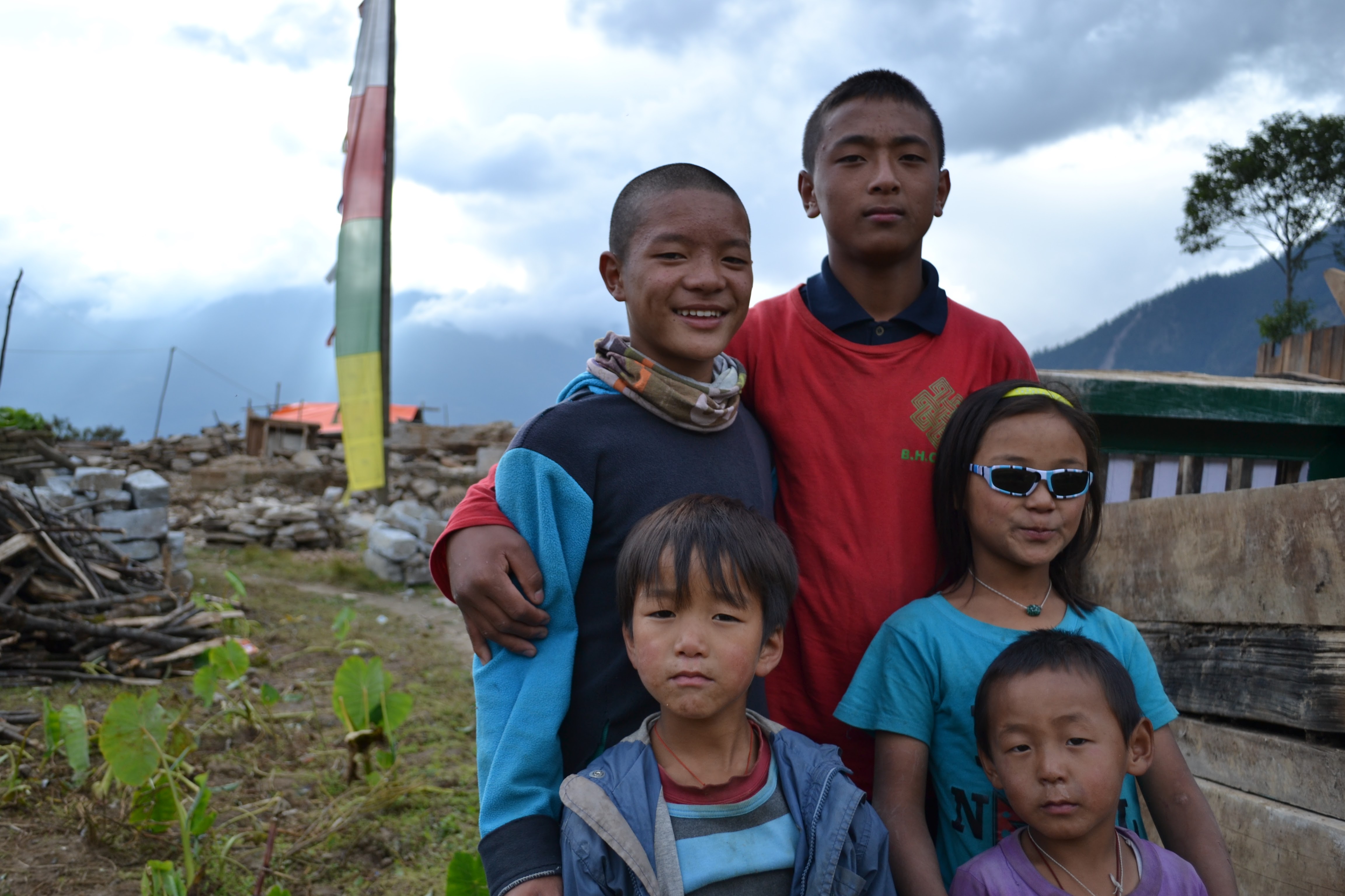 Local children and students pose together in front of a prayer flag in a Nepali village