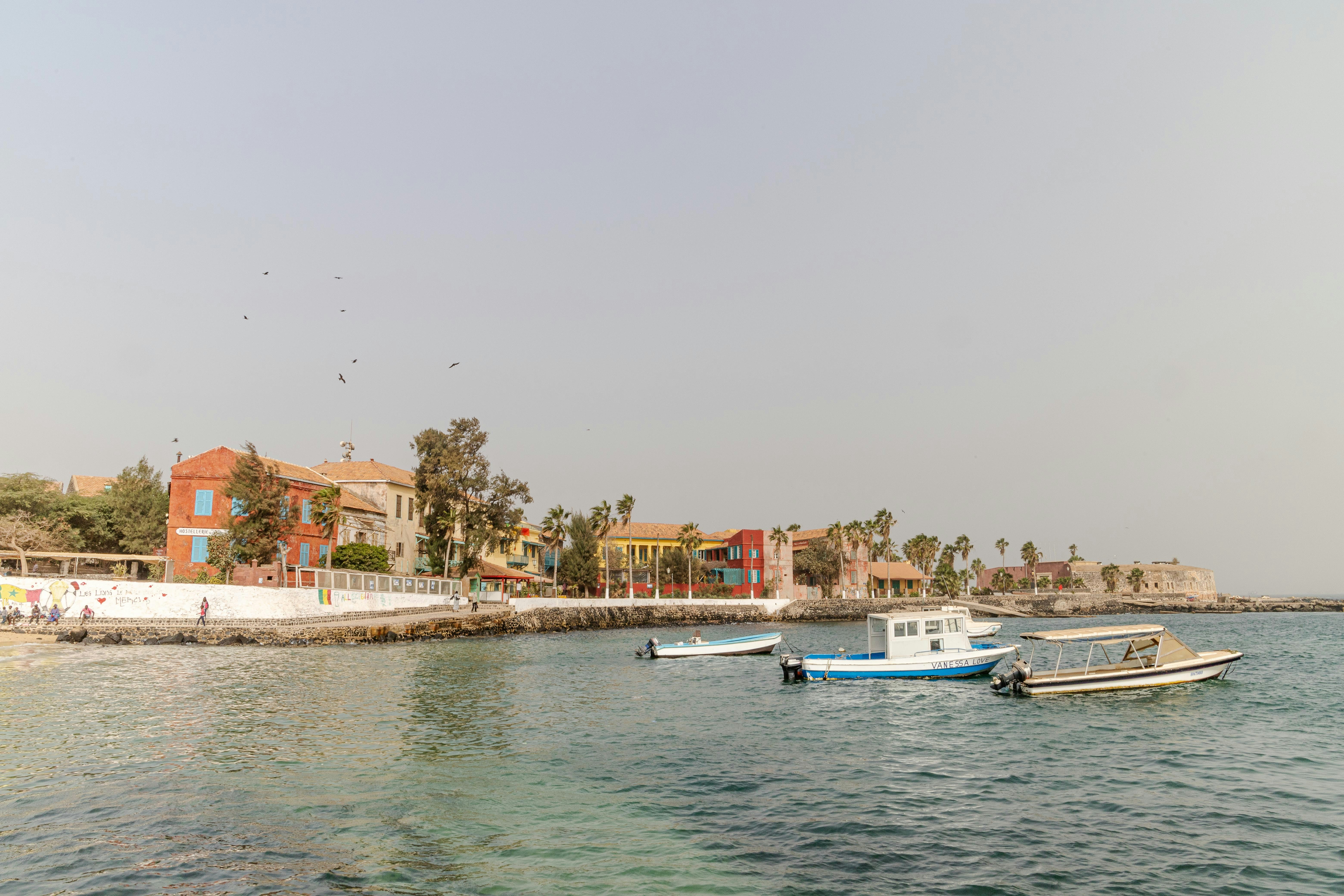 Colorful colonial-era buildings along a seawall, with small boats moored in the calm harbor.