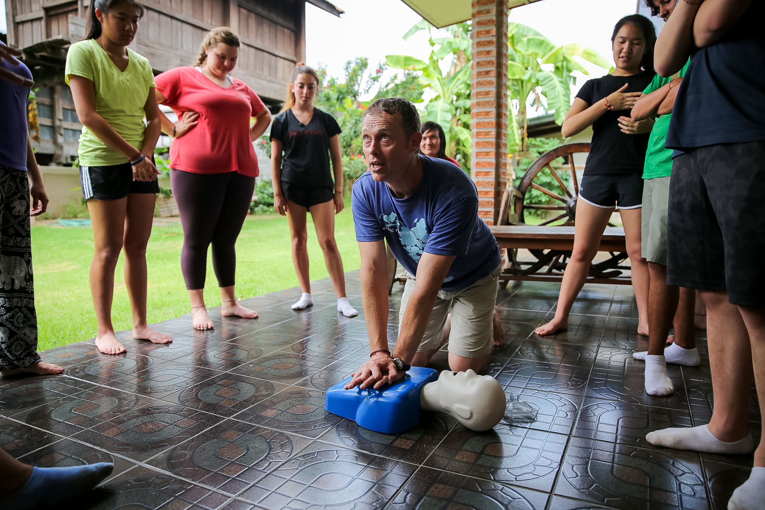 a group of people standing around a man demonstrating cpr on a mannequin