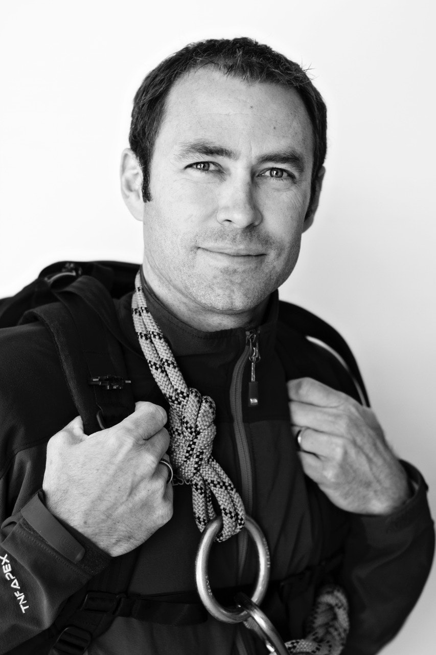 Black and white portrait of Dr. Will Smith, a search and rescue doctor, holding climbing rope and gear over his shoulder, highlighting his readiness for high-risk missions.
