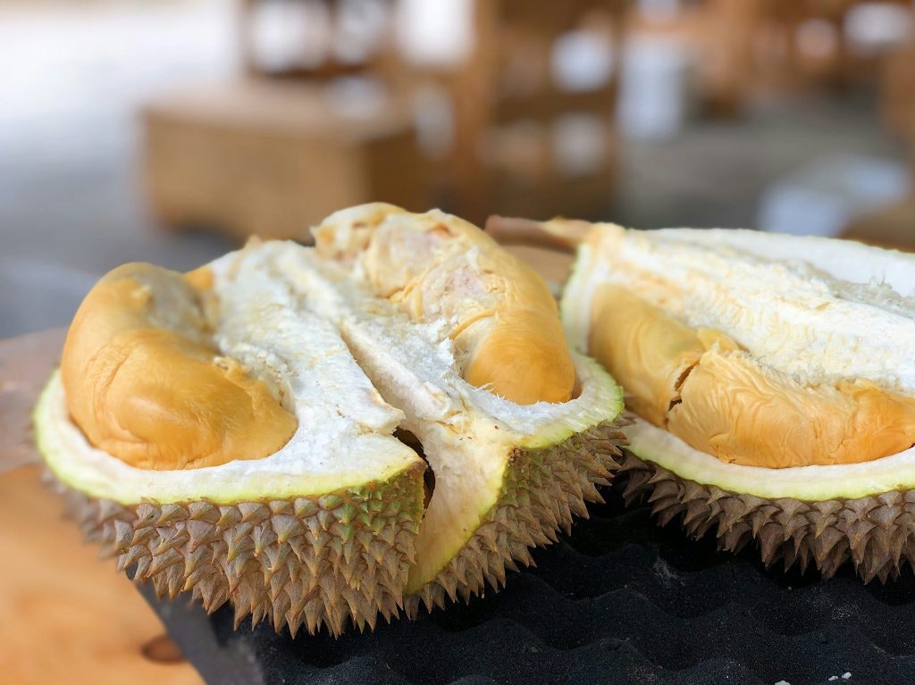Large durian cut in half on a table with the yellow fruit flesh still inside.