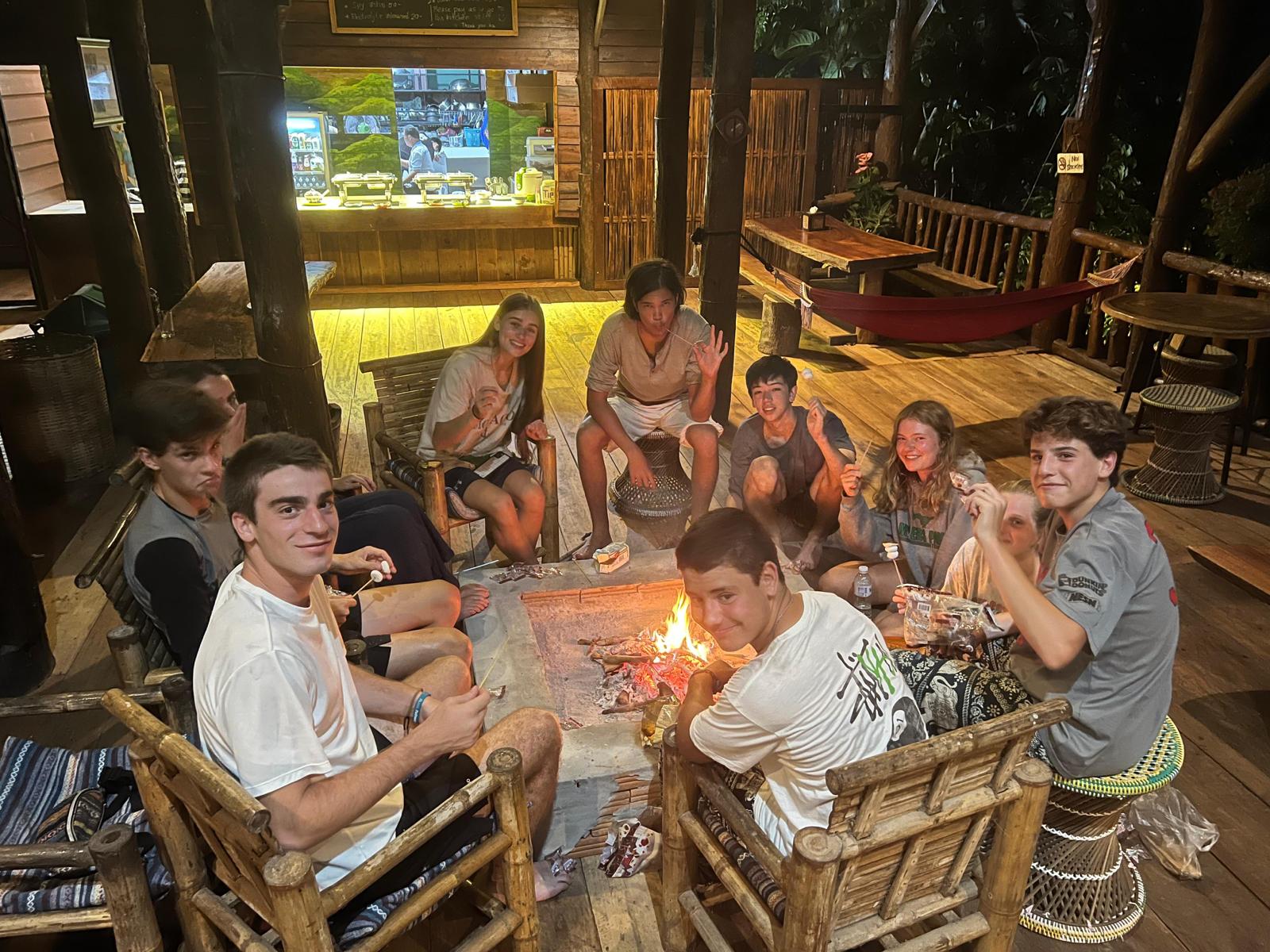 students enjoying a bonfire outside on wooden chairs