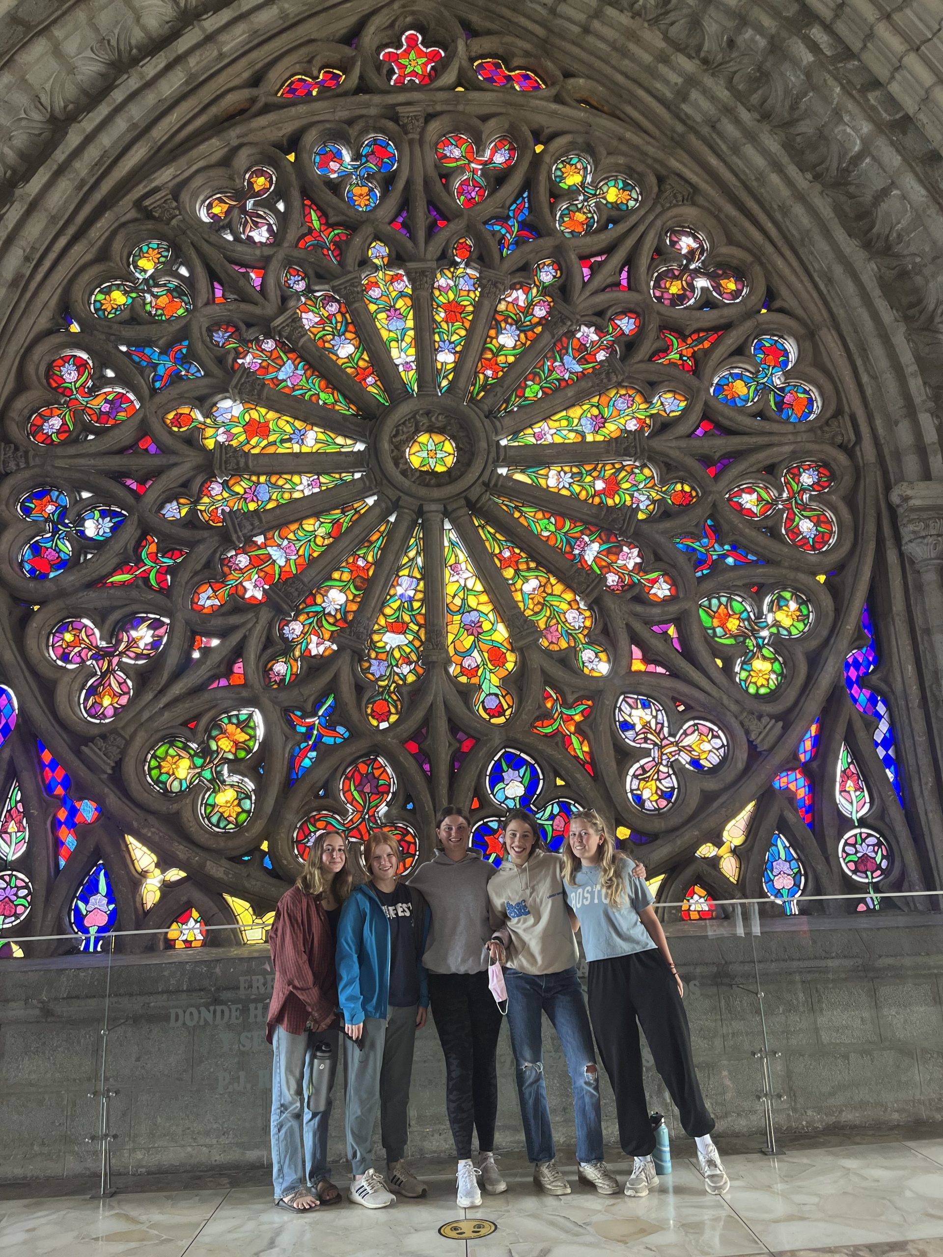 Students stand beneath a large stained-glass rose window inside a stone basilica in Quito.