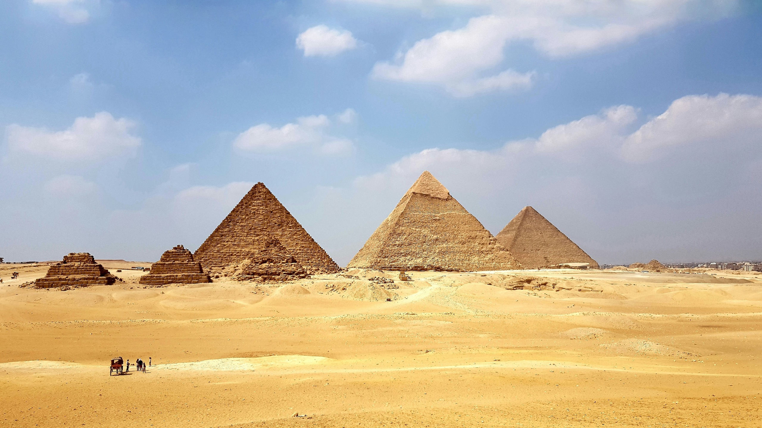 Pyramids stand on a sunlit plateau, the largest at left, under wisps of cloud.