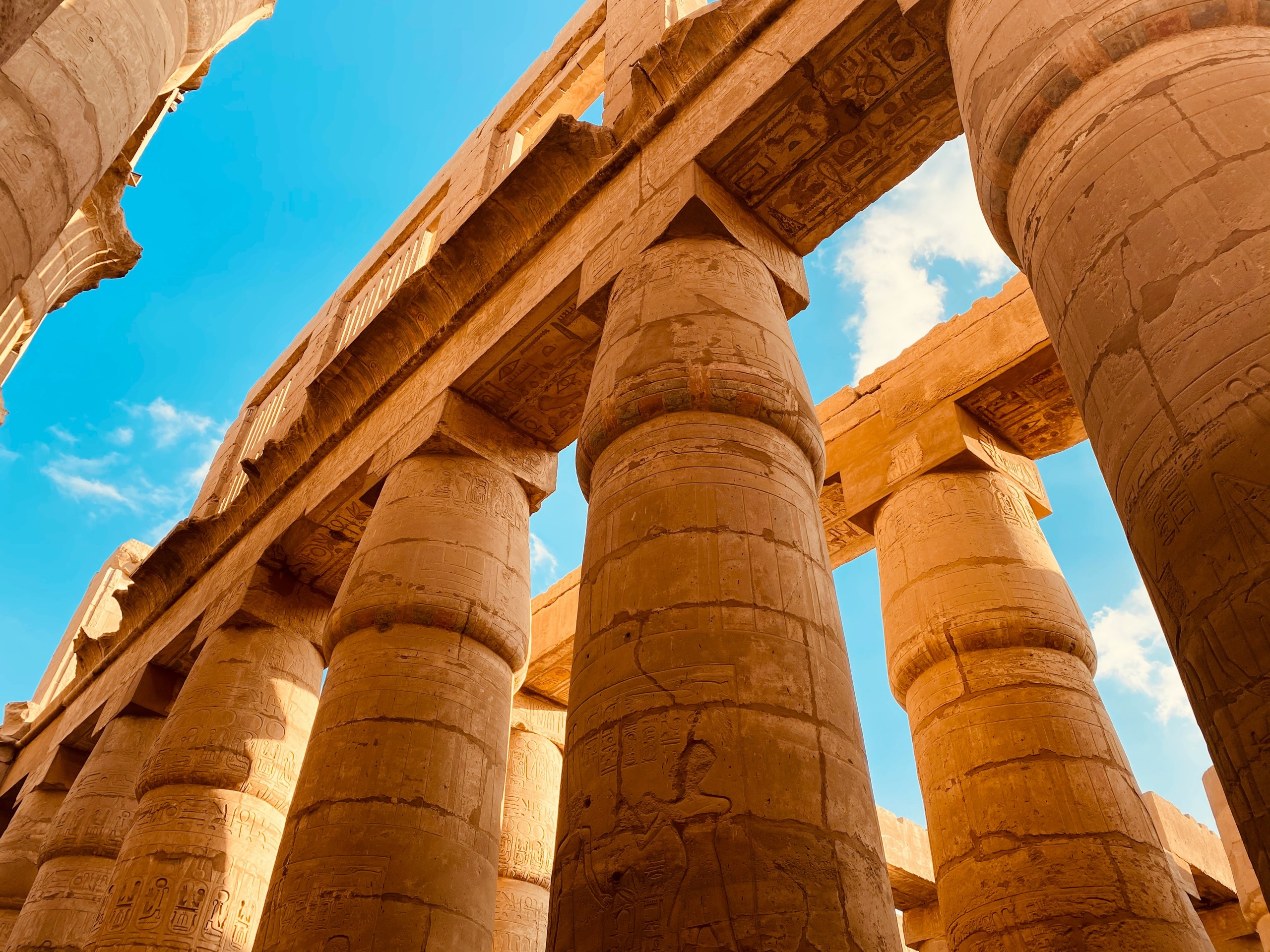 Massive sandstone columns of a temple hall, seen from below against a blue sky.