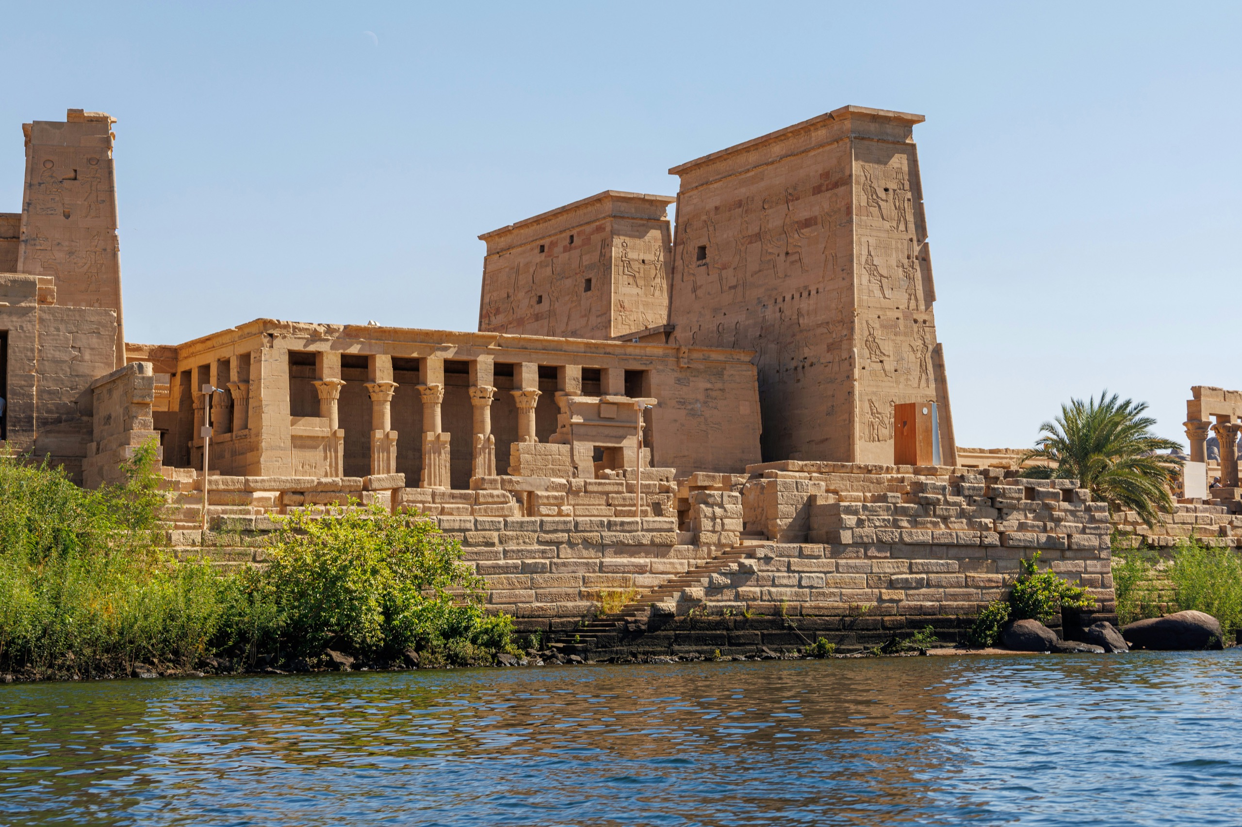 A colonnaded island temple stands at the water's edge under a blue sky.