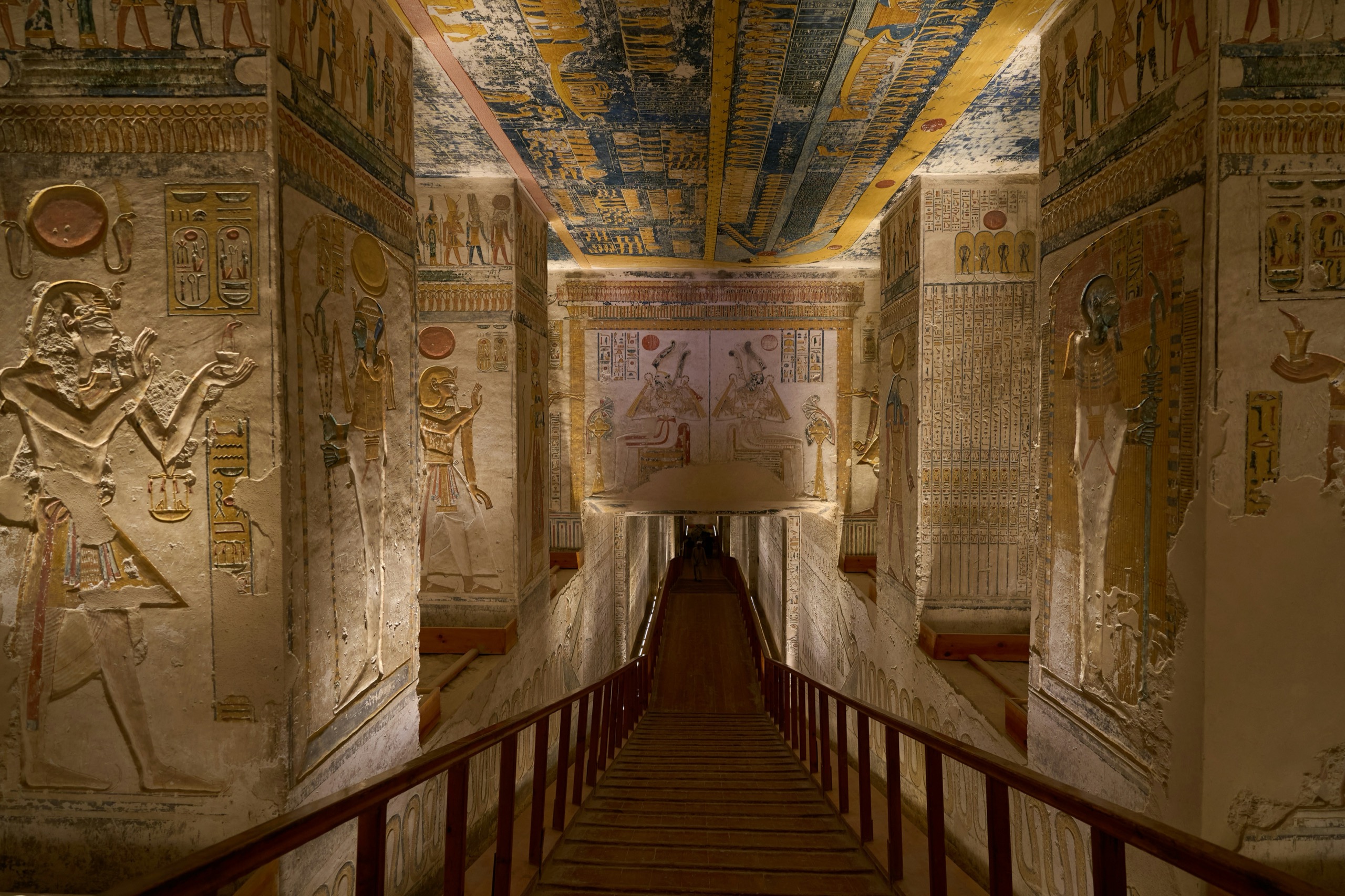 A stone stairway descends into a painted tomb corridor lined with carved hieroglyphs.