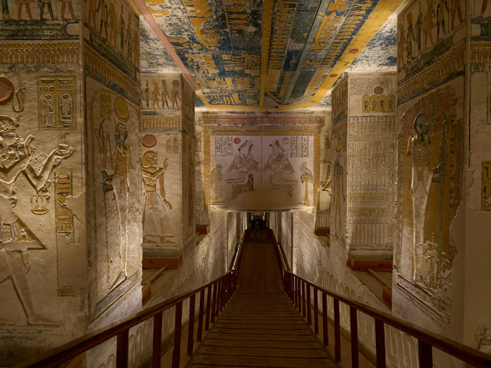 A stone stairway descends into a painted tomb corridor lined with carved hieroglyphs.