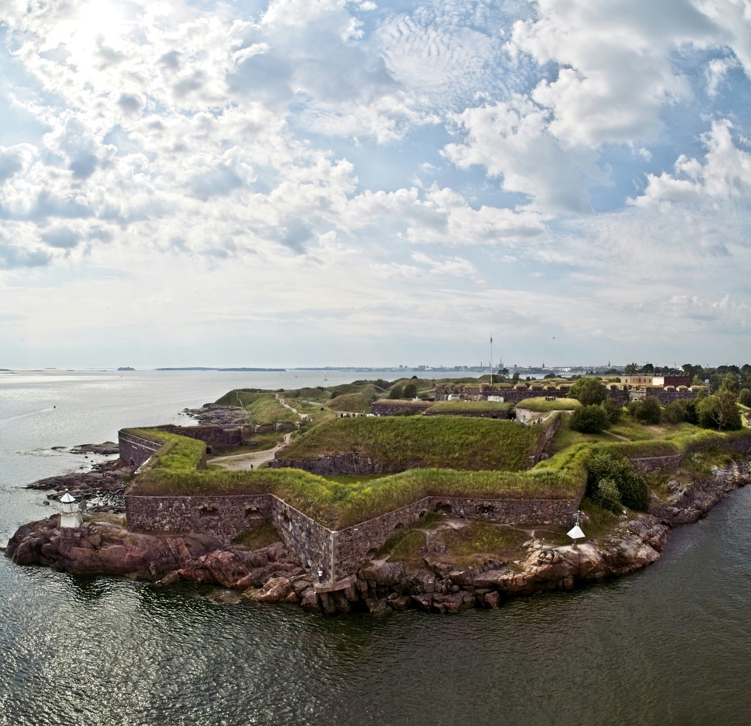 A star-shaped stone sea fortress on a green island, seen from the water under a broken sky.