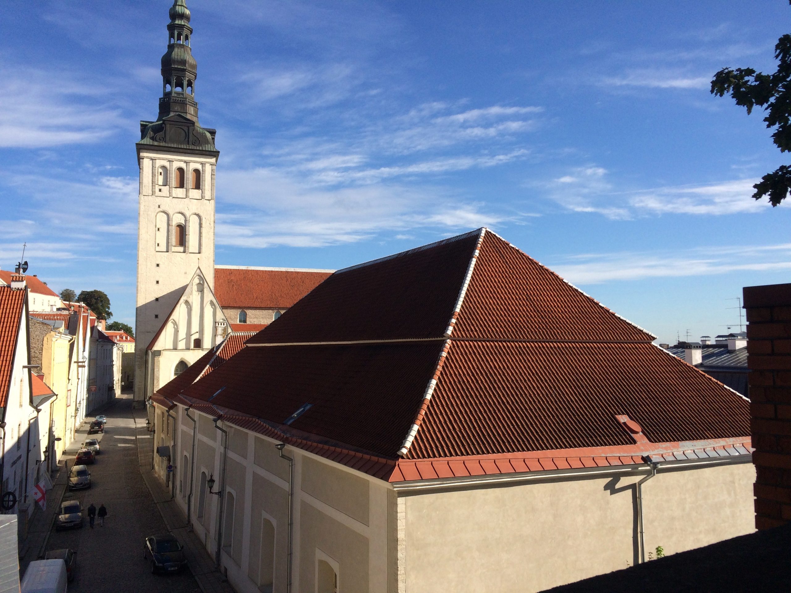A Gothic church spire and red-tile roofs cluster below a wide blue sky, seen from a hillside viewpoint