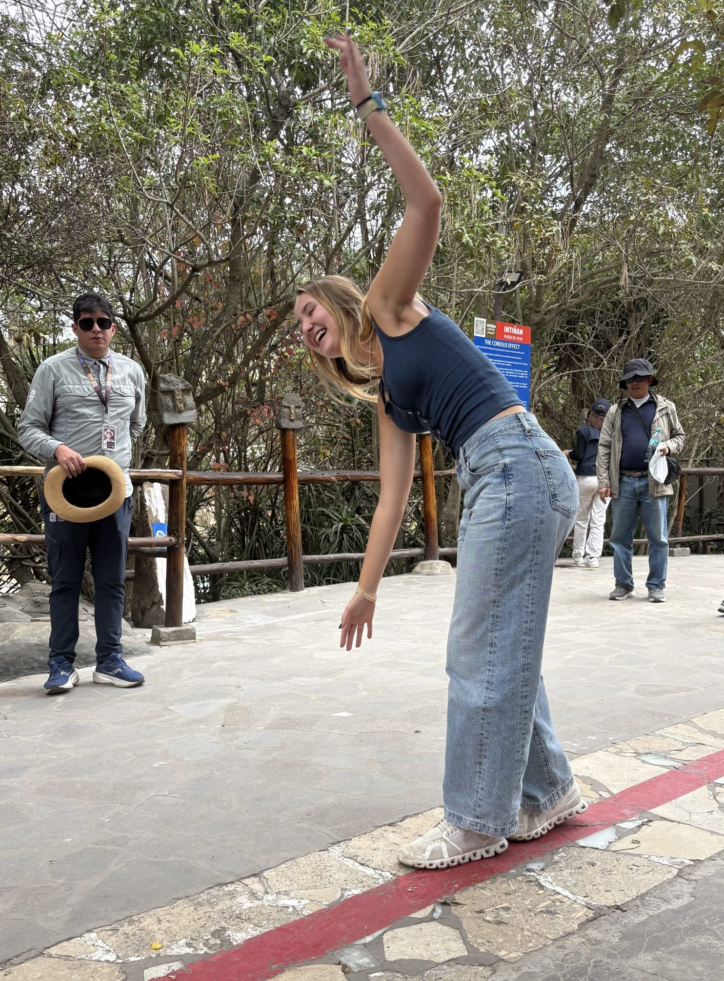 A student balances along the painted equator line at Mitad del Mundo, arms out, with staff watching from the rail.