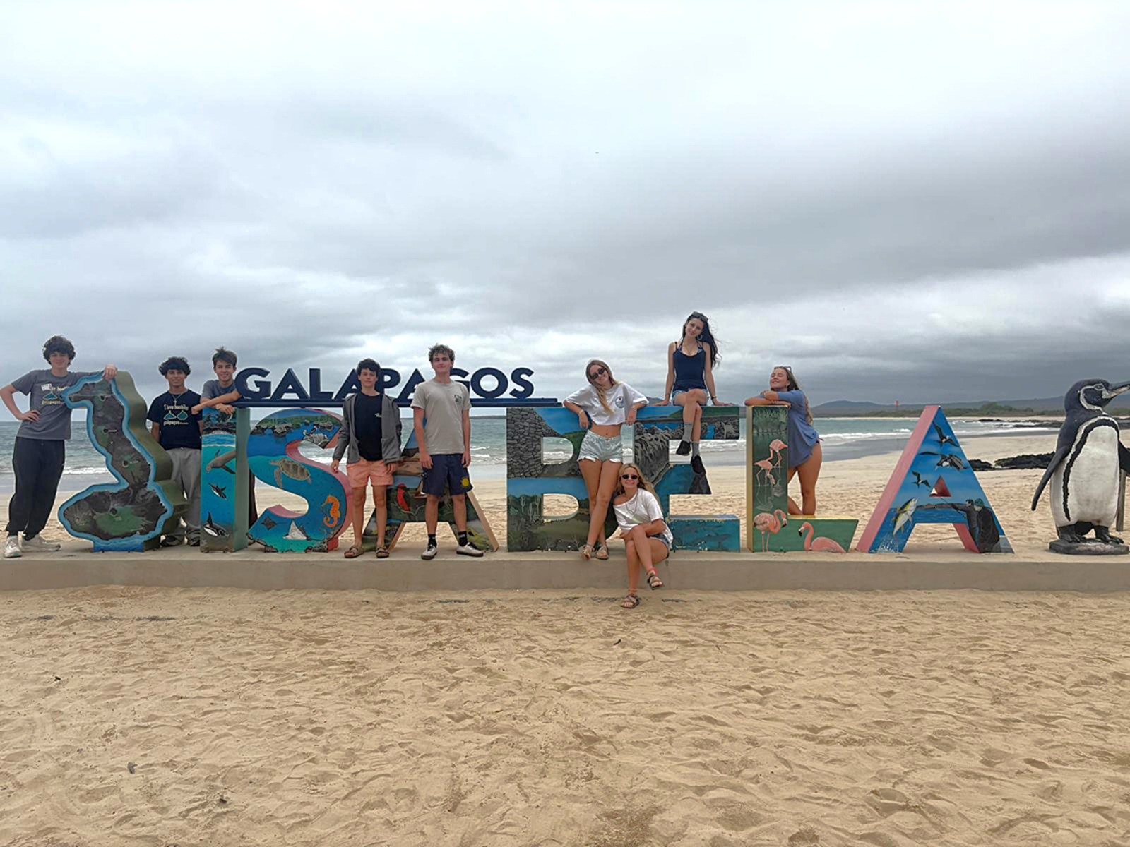 Students pose in Ecuador on a beach beside a large painted Galápagos Isabela sign