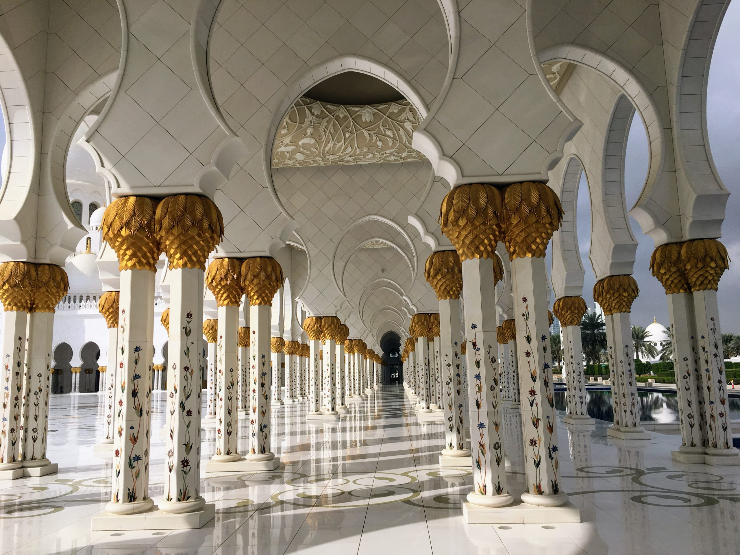 Ornate golden palm-shaped columns lining the white marble courtyard of the Sheikh Zayed Grand Mosque in Abu Dhabi