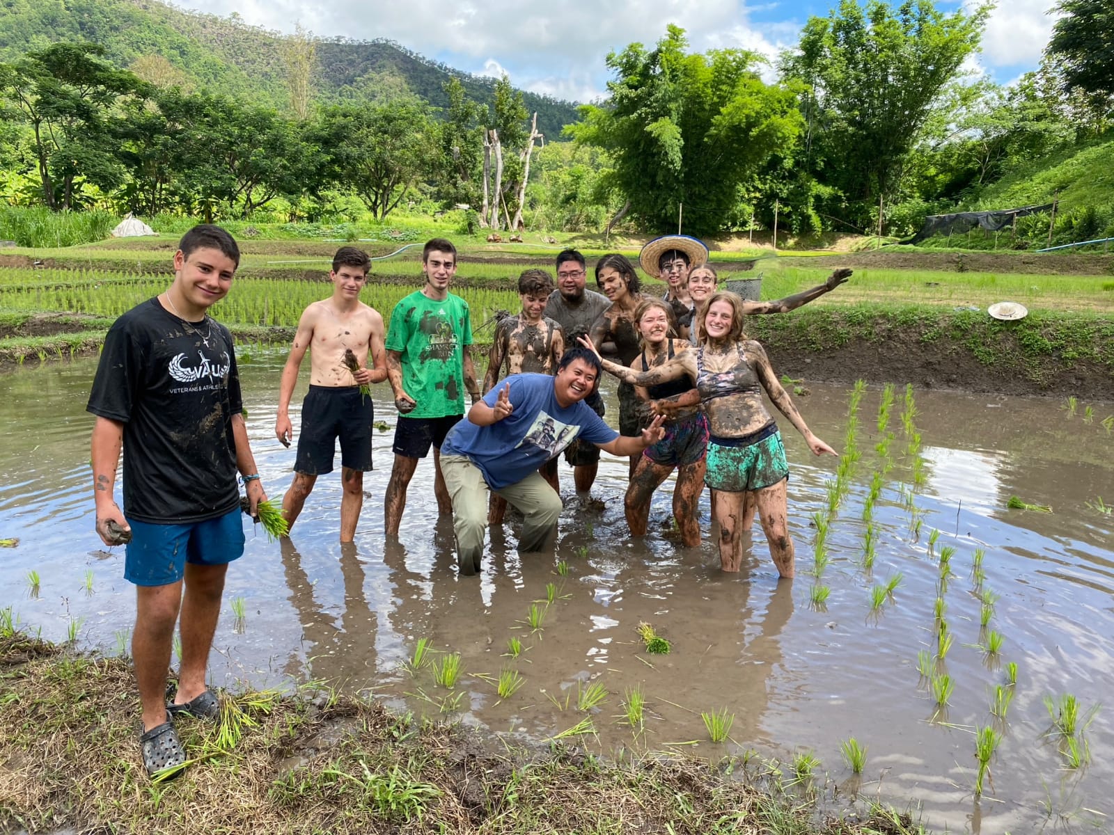 students outside in the field standing in the muddy rice water