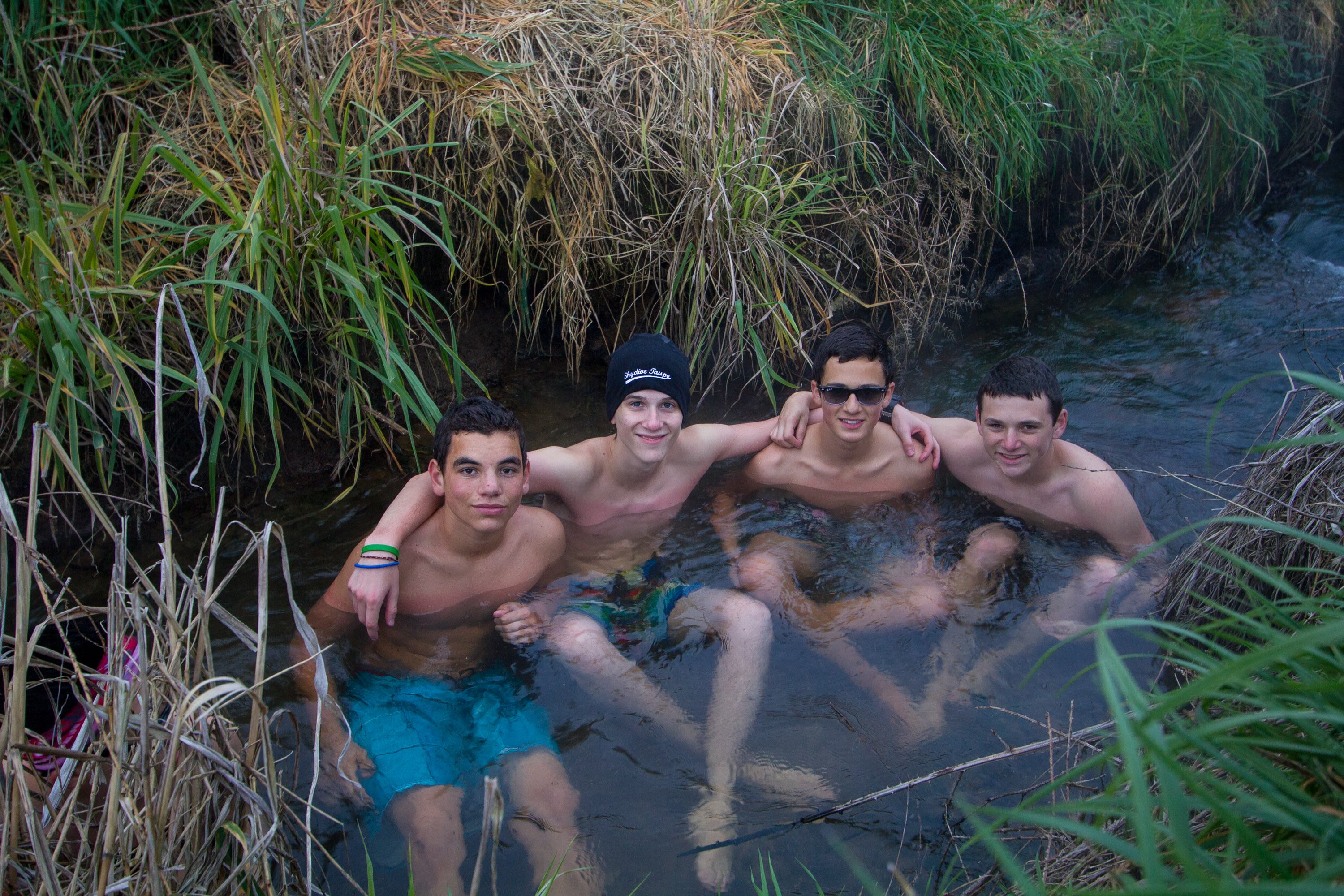 Students relax together in a shallow stream surrounded by tall grass