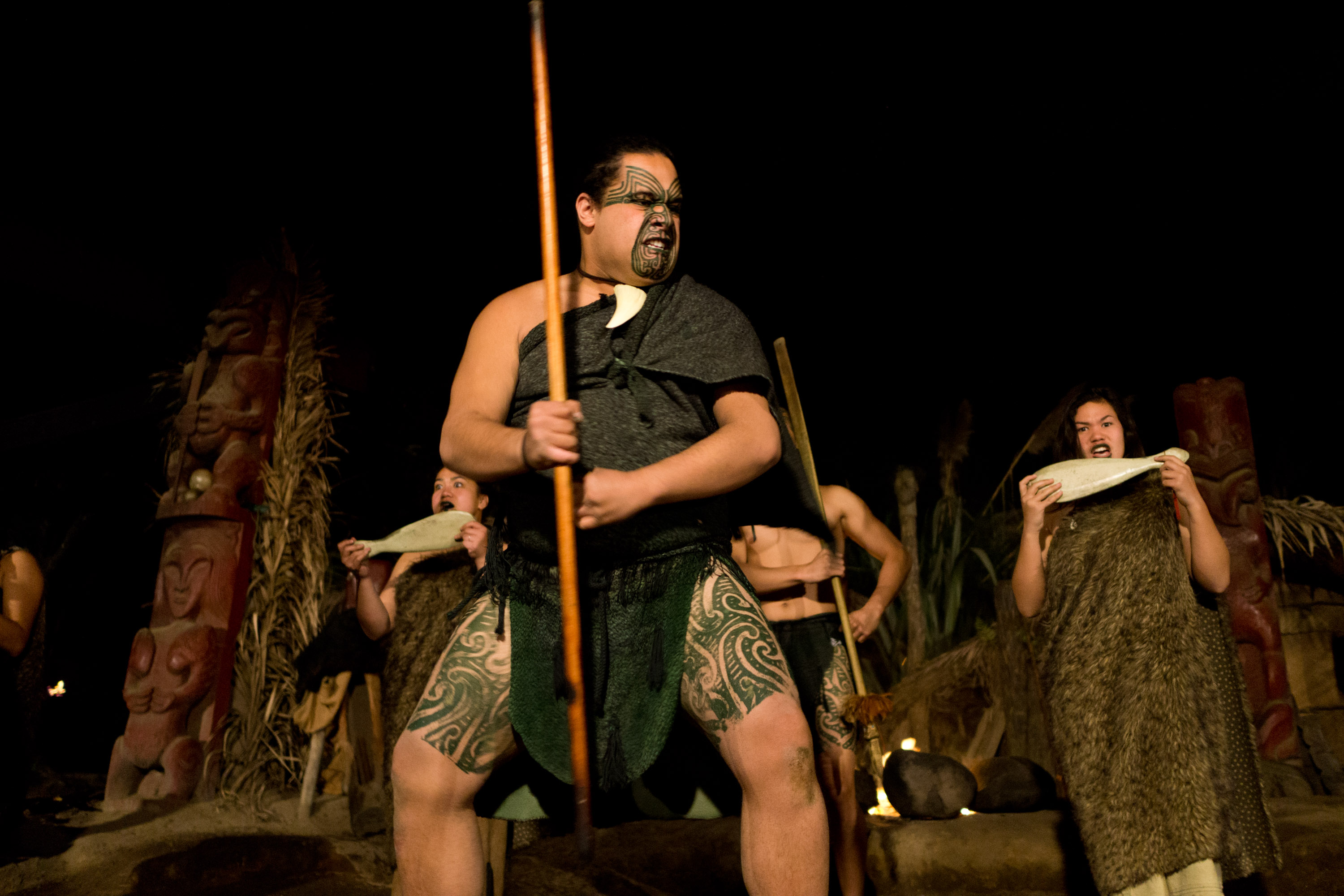 A performer in traditional Maori dress holds a taiaha during a nighttime cultural performance in New Zealand