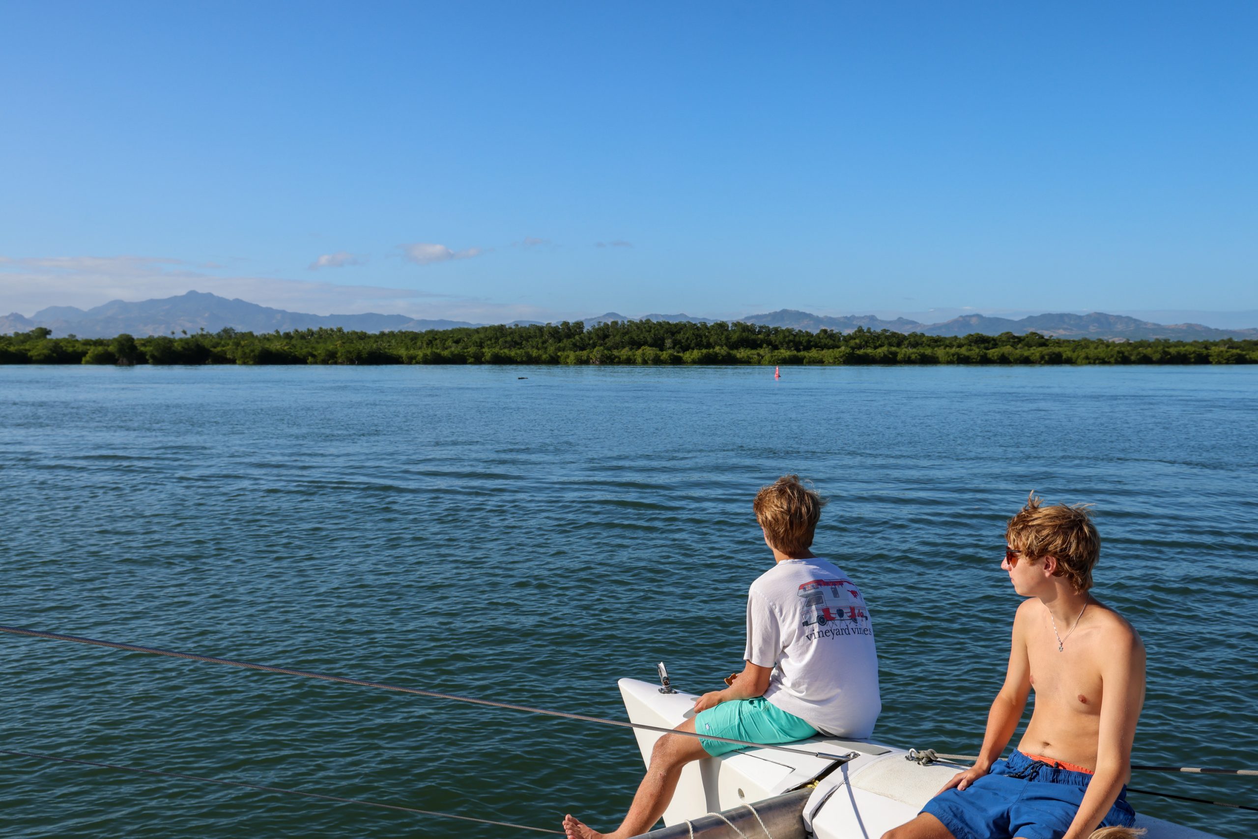 Students sit on a boat's bow watching the calm water and distant hills in Fiji