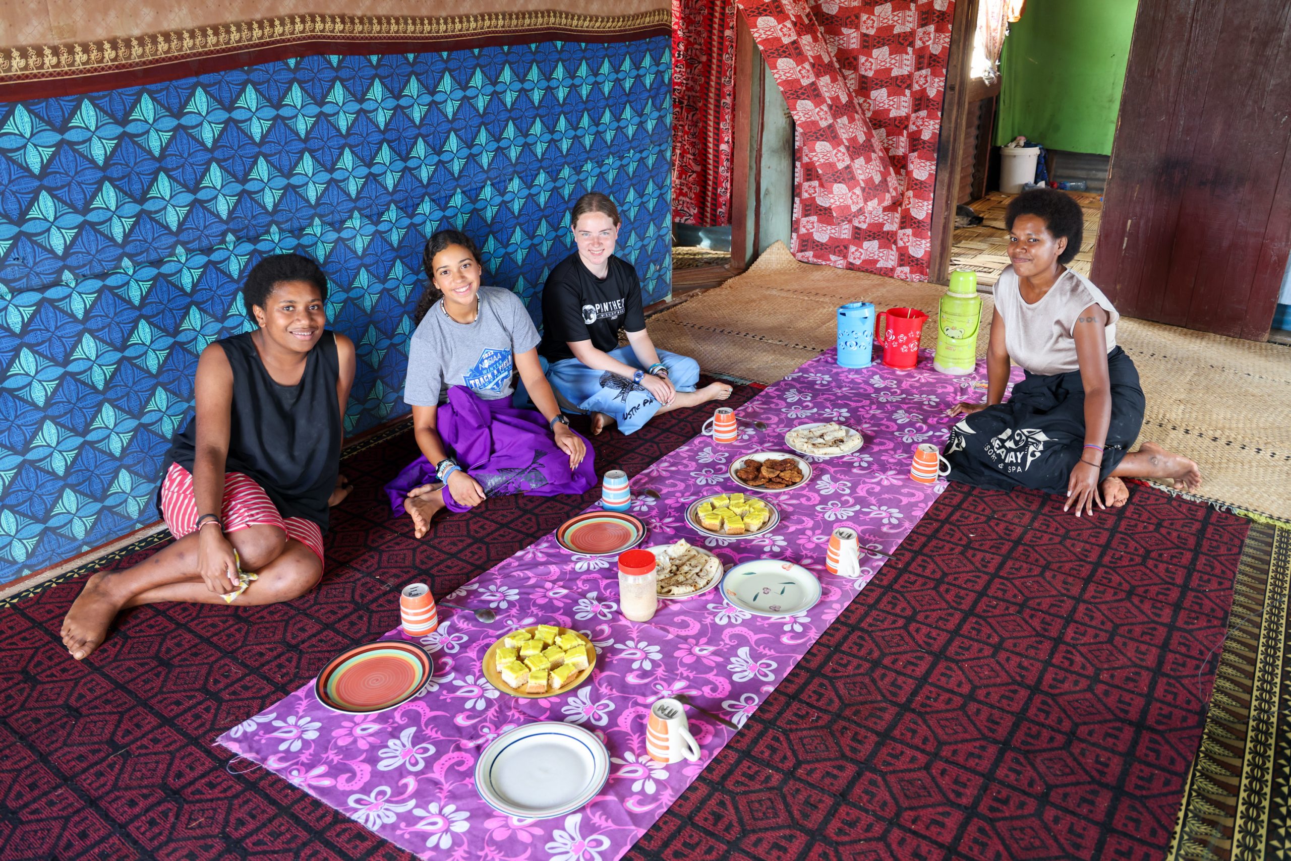 Students and hosts share a meal seated on woven mats in a Fijian home