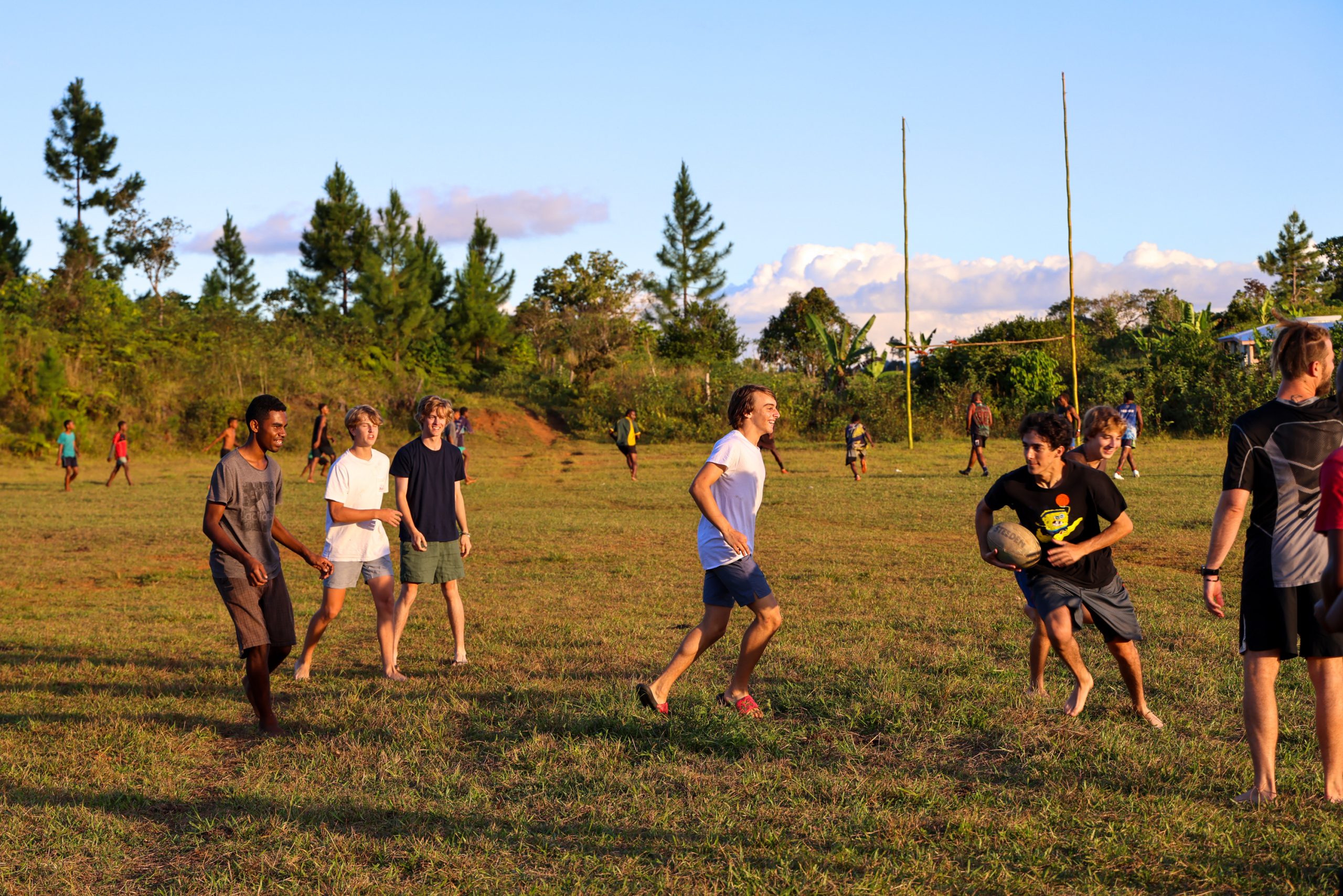 Students play a game of touch rugby on a grass field at sunset