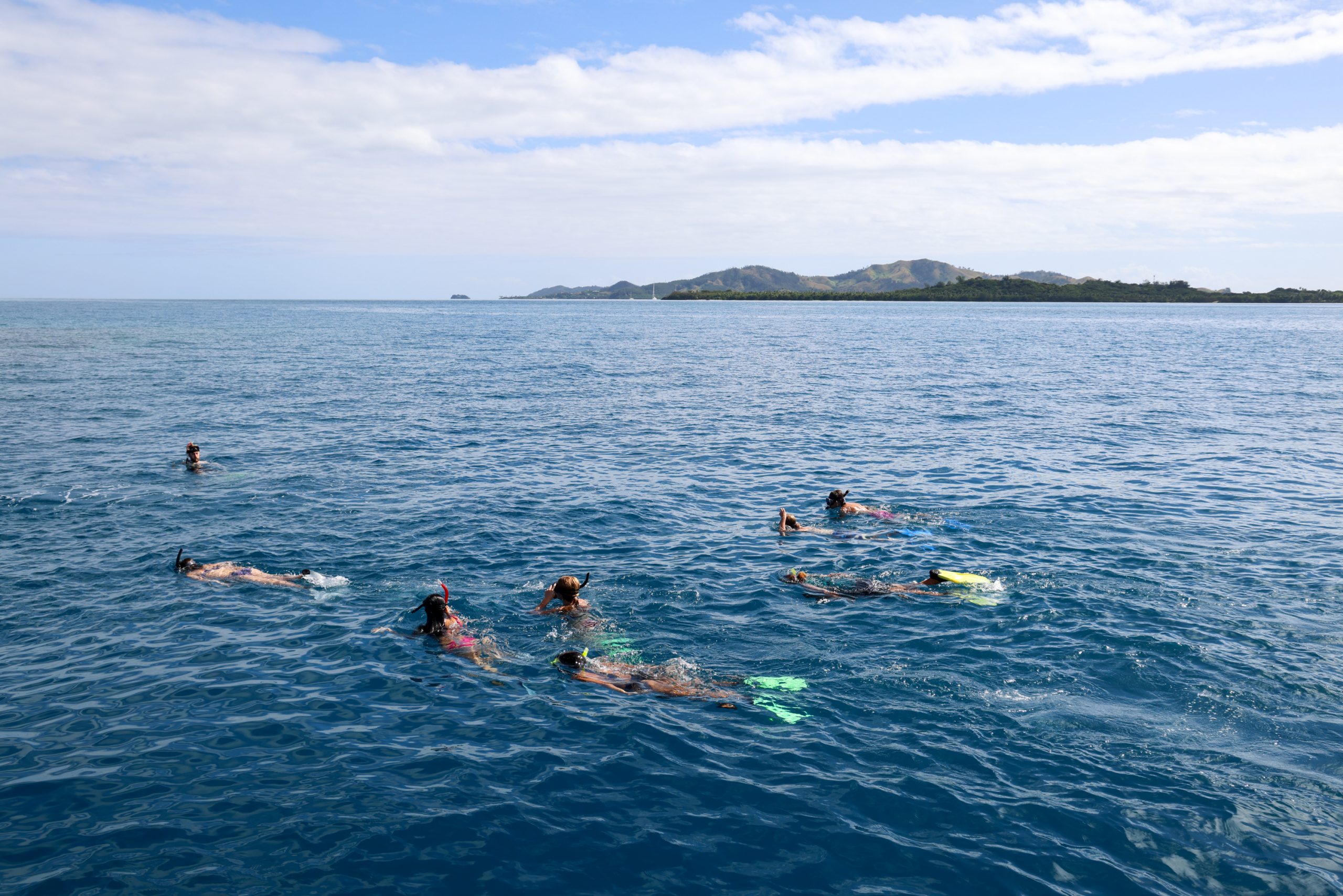 Snorkelers float along the ocean surface with hills in the distance