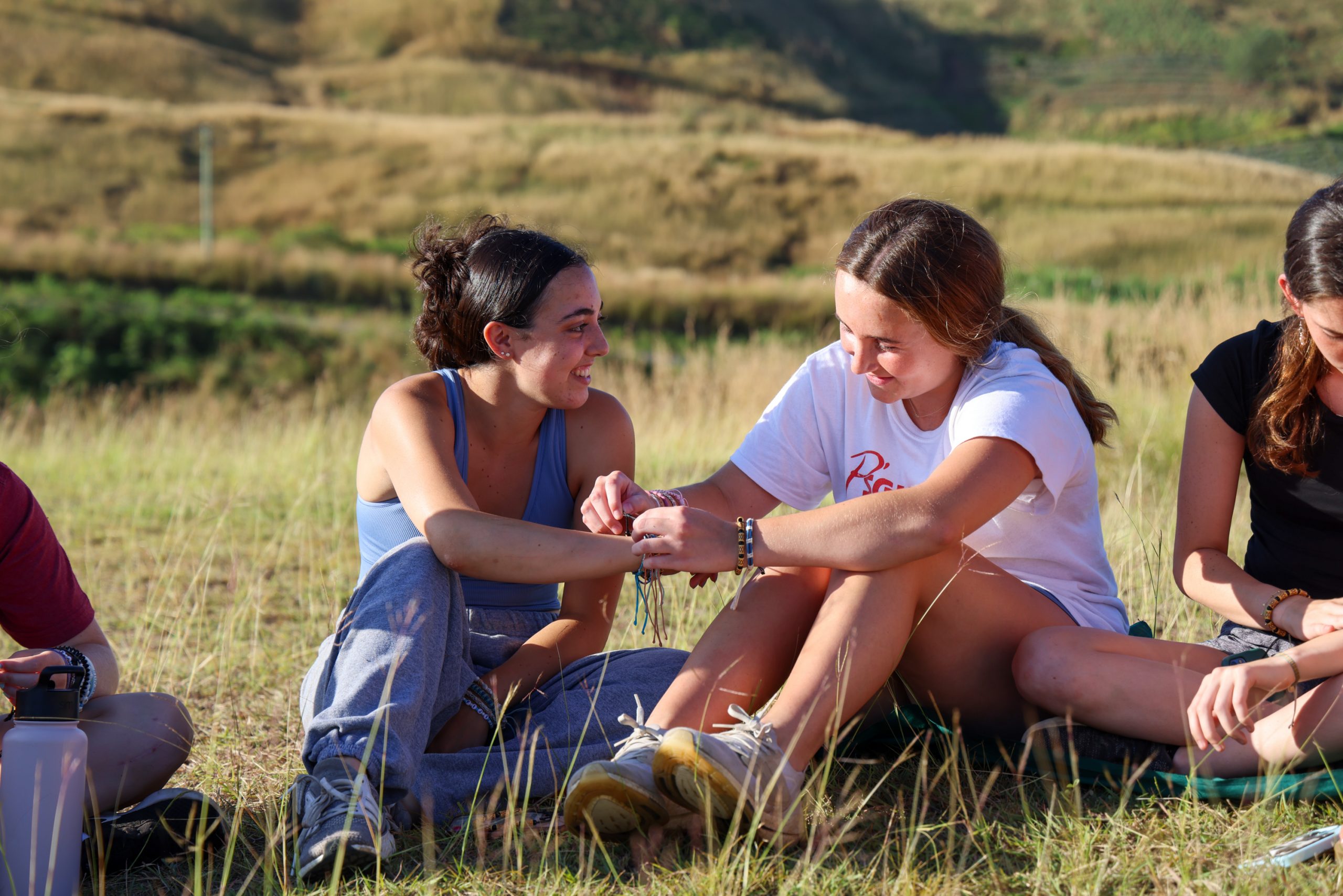 Students share a laugh while sitting together in a grassy field