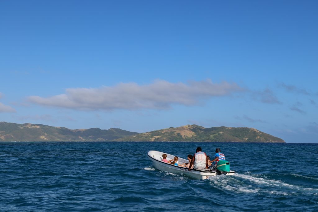 Small boat carrying people across the blue waters of Fiji with islands in the background.