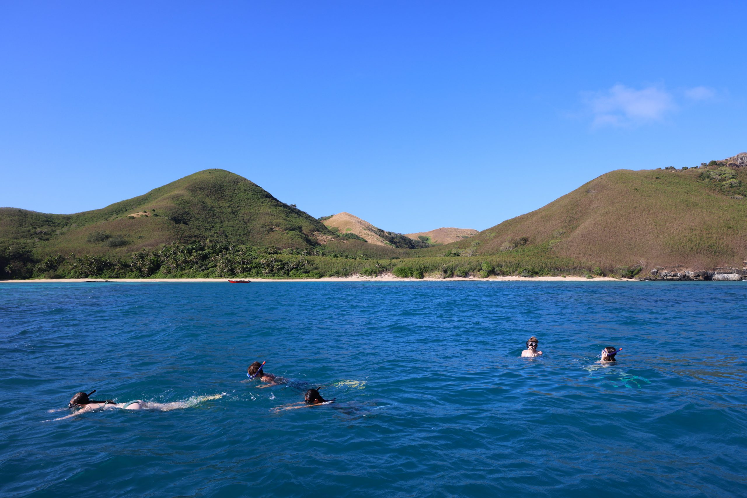 Students snorkel in calm coastal waters below green island hills