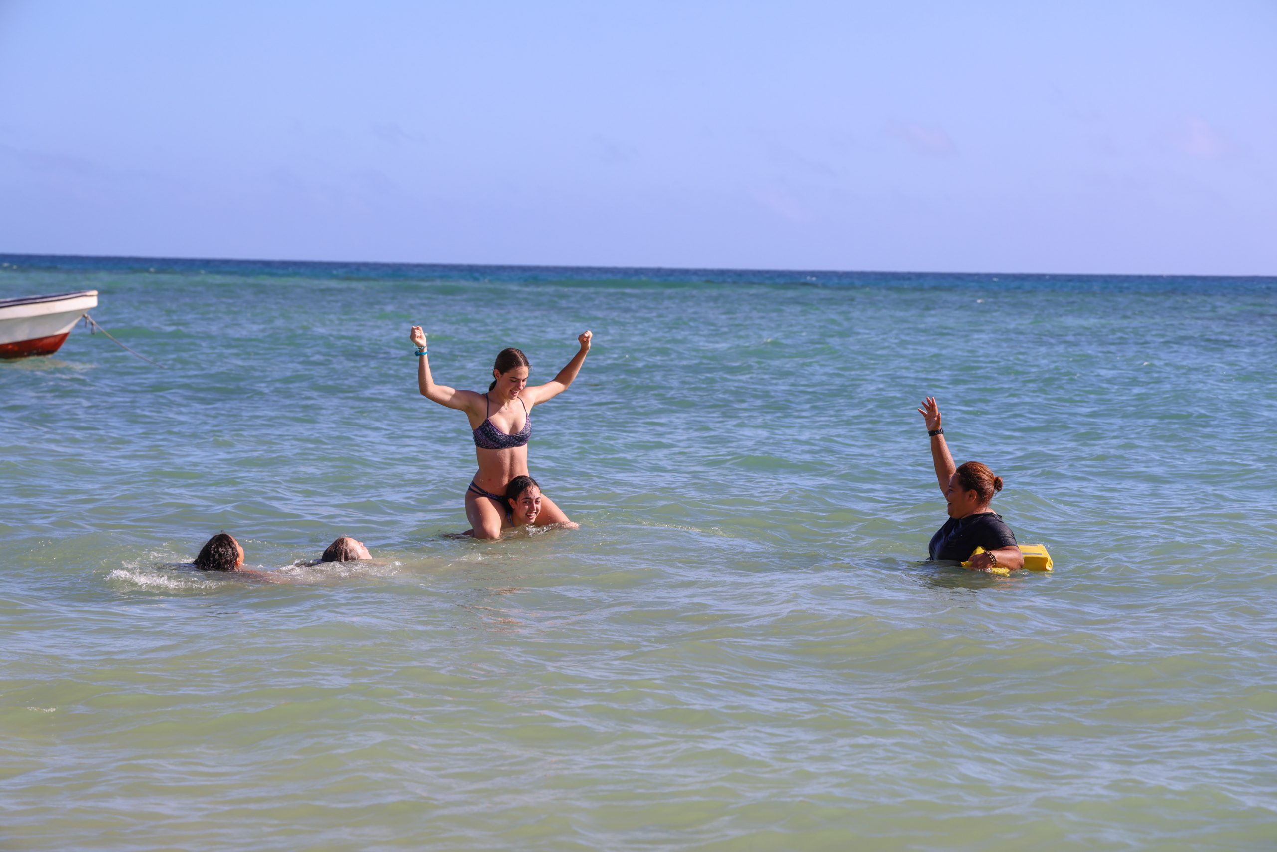 Students play and swim in the ocean near a boat