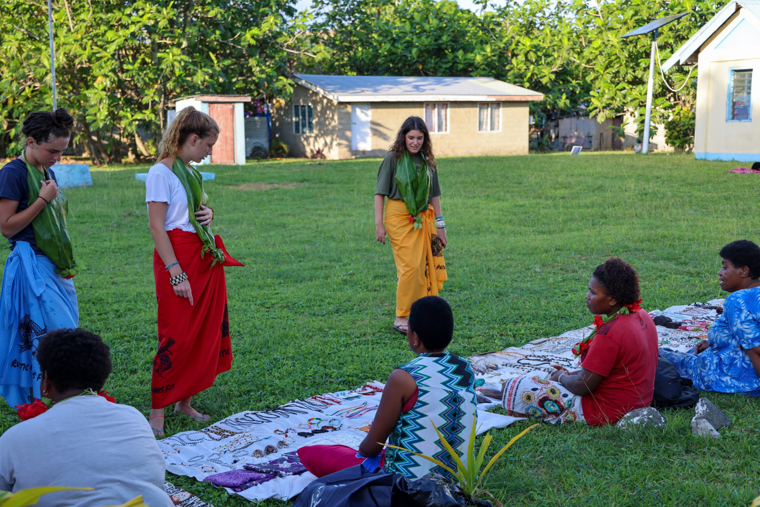 Students take part in a traditional welcome ceremony with local hosts on a grassy village lawn