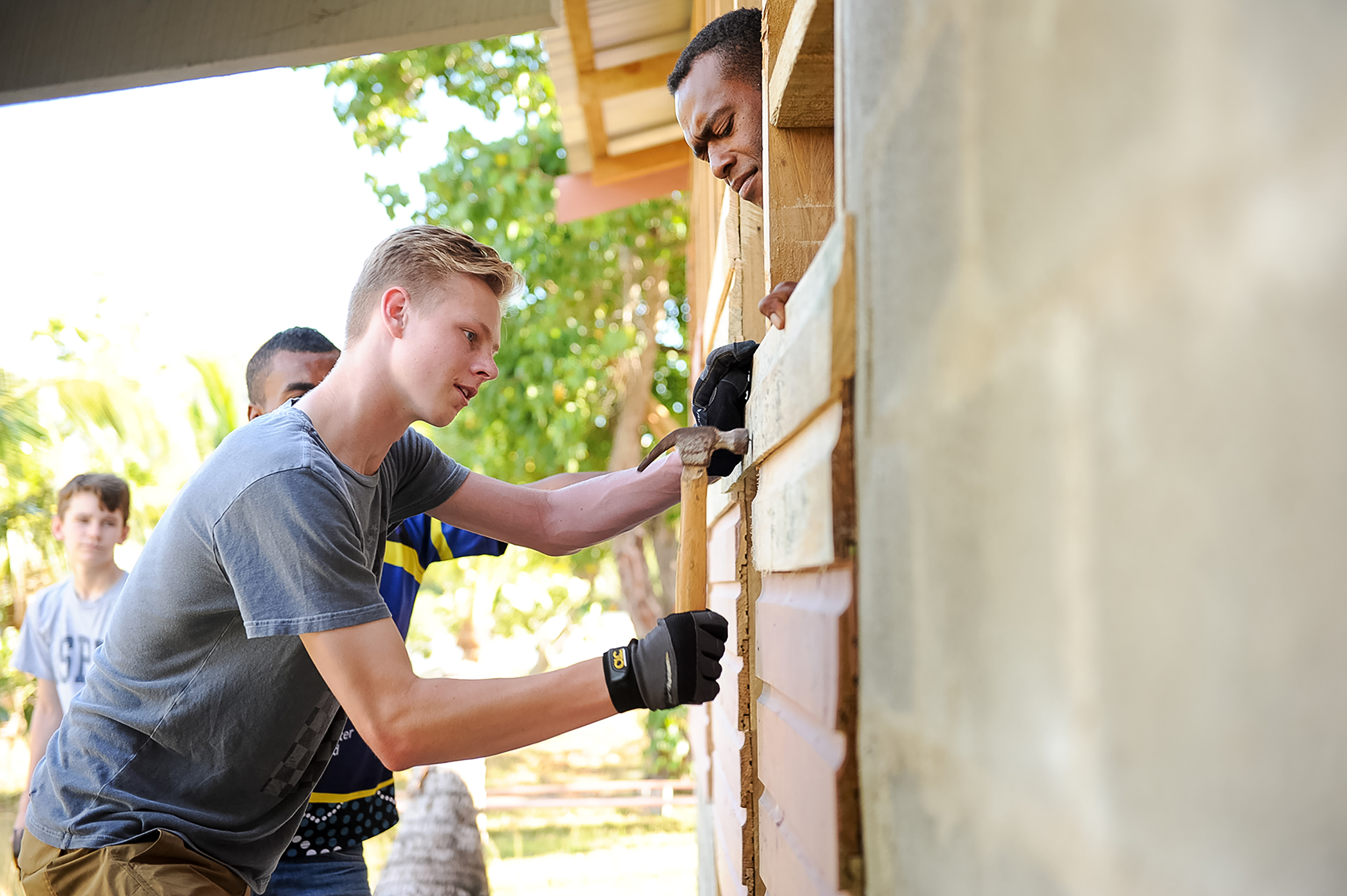A student helps apply plaster to a building wall during a community service project