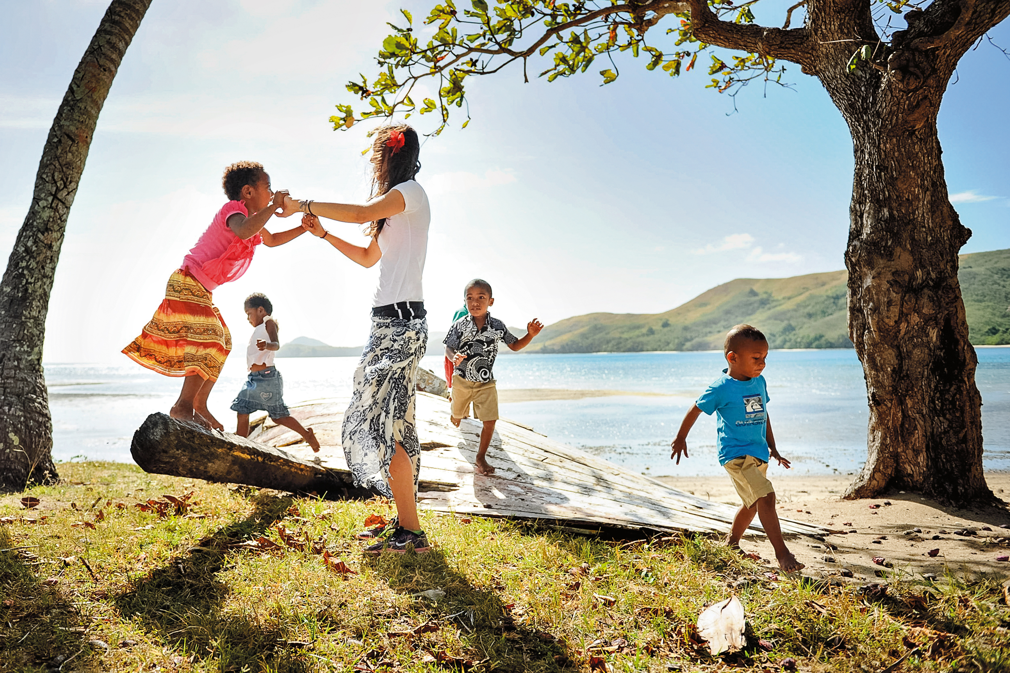 A student plays with local children on a shaded beach near the water