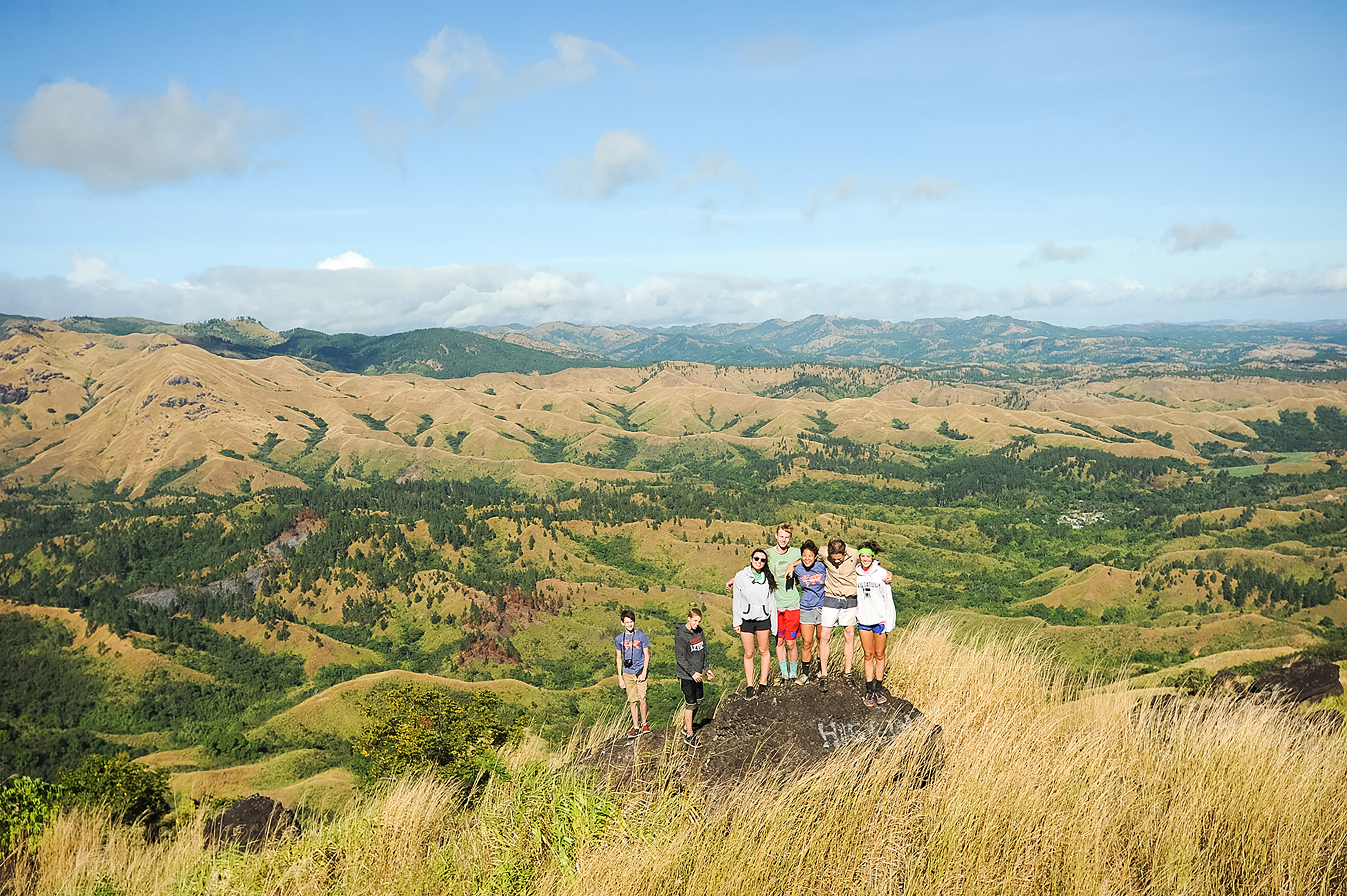 Students gather atop a rocky overlook above rolling green hills in Fiji