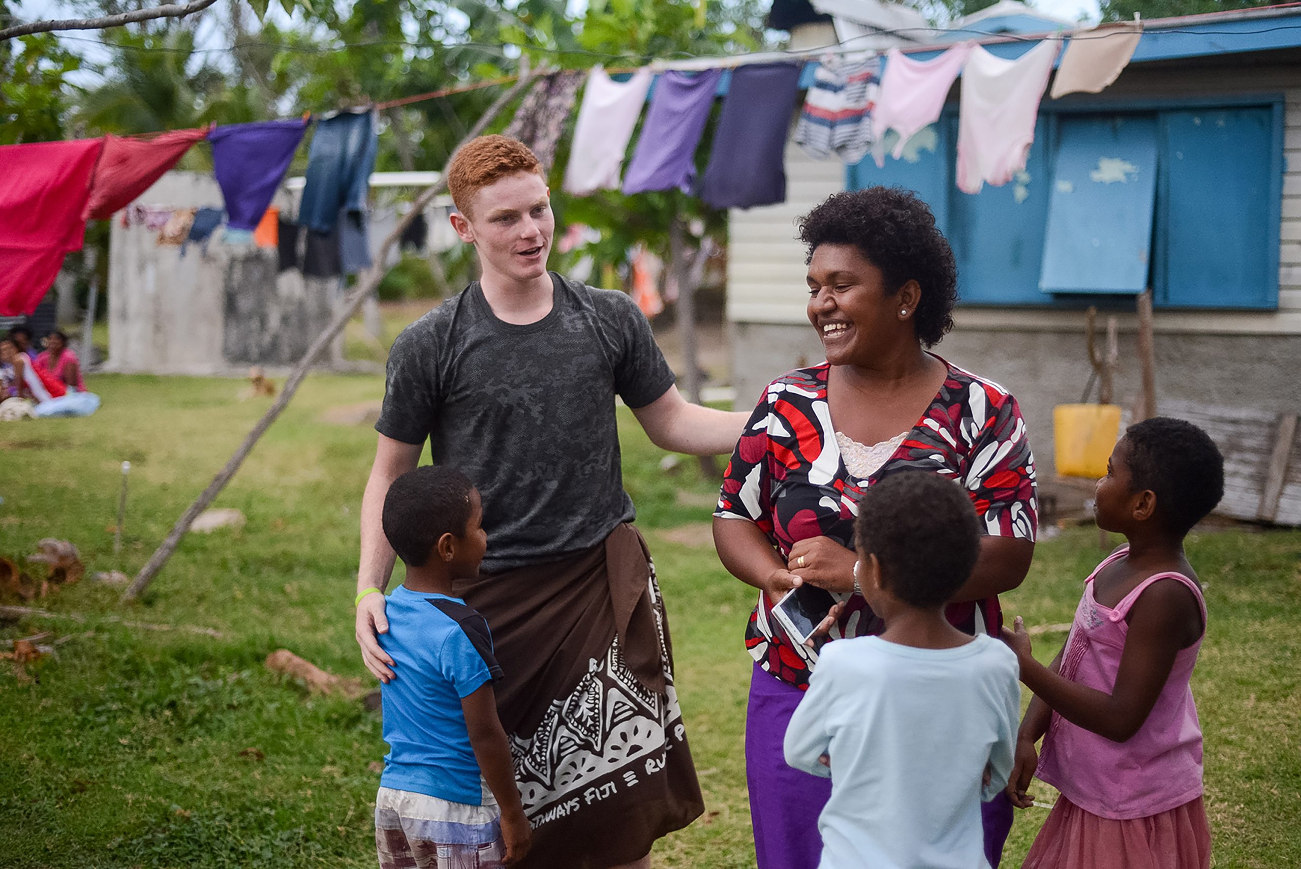Student sharing a laugh with a host family in a Pacific island village during a Rustic Pathways volunteer abroad in the Pacific cultural exchange program.
