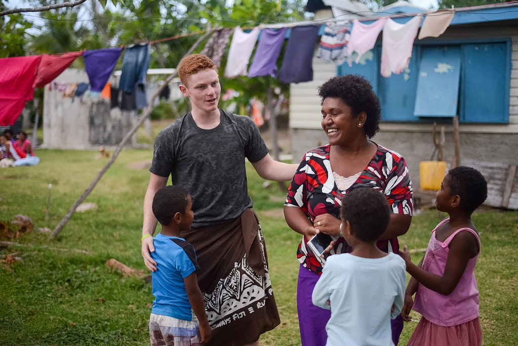 Student sharing a laugh with a host family in a Pacific island village during a Rustic Pathways volunteer abroad in the Pacific cultural exchange program.